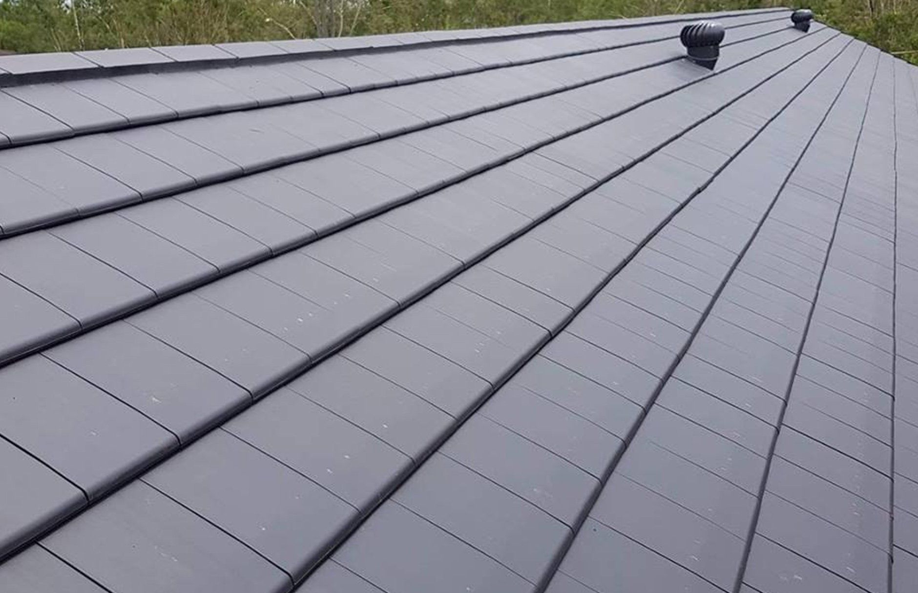 A close up of a black roof with a vent on it.