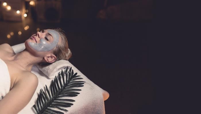 Woman with a face mask relaxing on a spa bed. Dark setting, string lights in background.