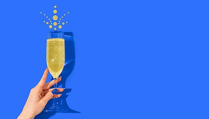 Hand holding a champagne flute with bubbles and a Cardano logo above, on a blue background.