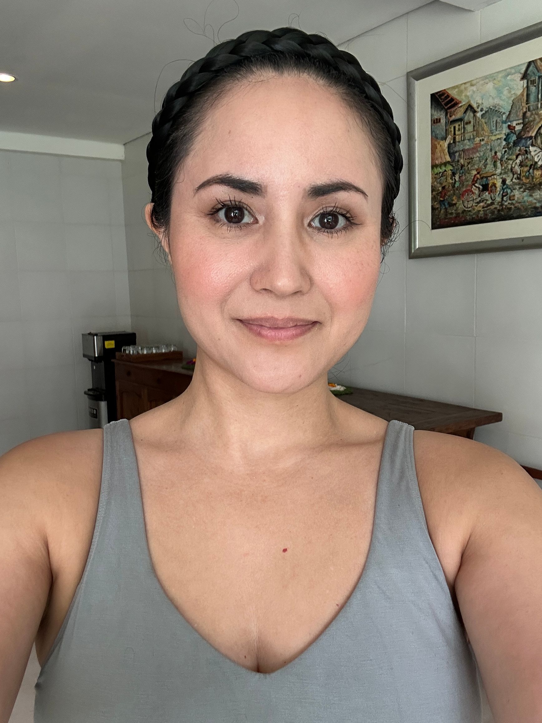 Woman with braided hair smiling, wearing a gray tank top, indoors.