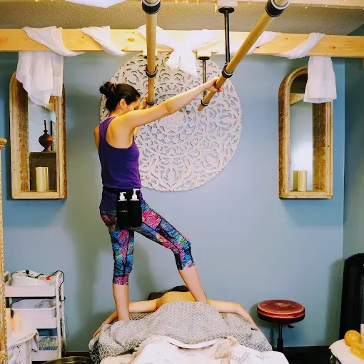 Woman performing Thai massage, using bars for balance, on a client in a spa-like room.