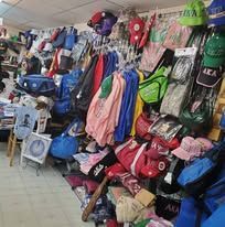 A wall of hanging backpacks, bags, and clothing in a crowded market stall