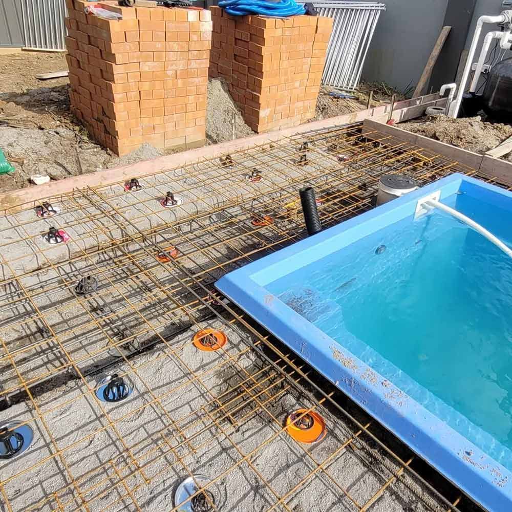 A Blue Swimming Pool is Being Built Next to a Brick Wall — Dave Smith Concrete in Salt Ash, NSW