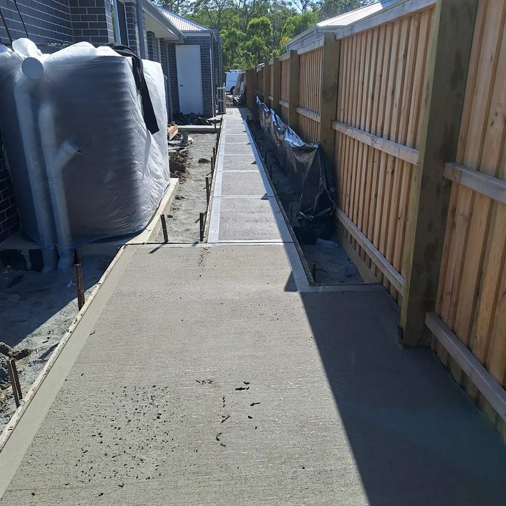 A Concrete Walkway With a Wooden Fence in the Background — Dave Smith Concrete in Salt Ash, NSW