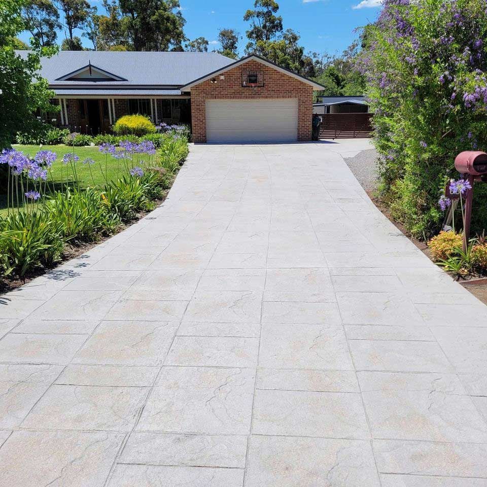 A Driveway Leading to a House With Purple Flowers — Dave Smith Concrete in Salt Ash, NSW