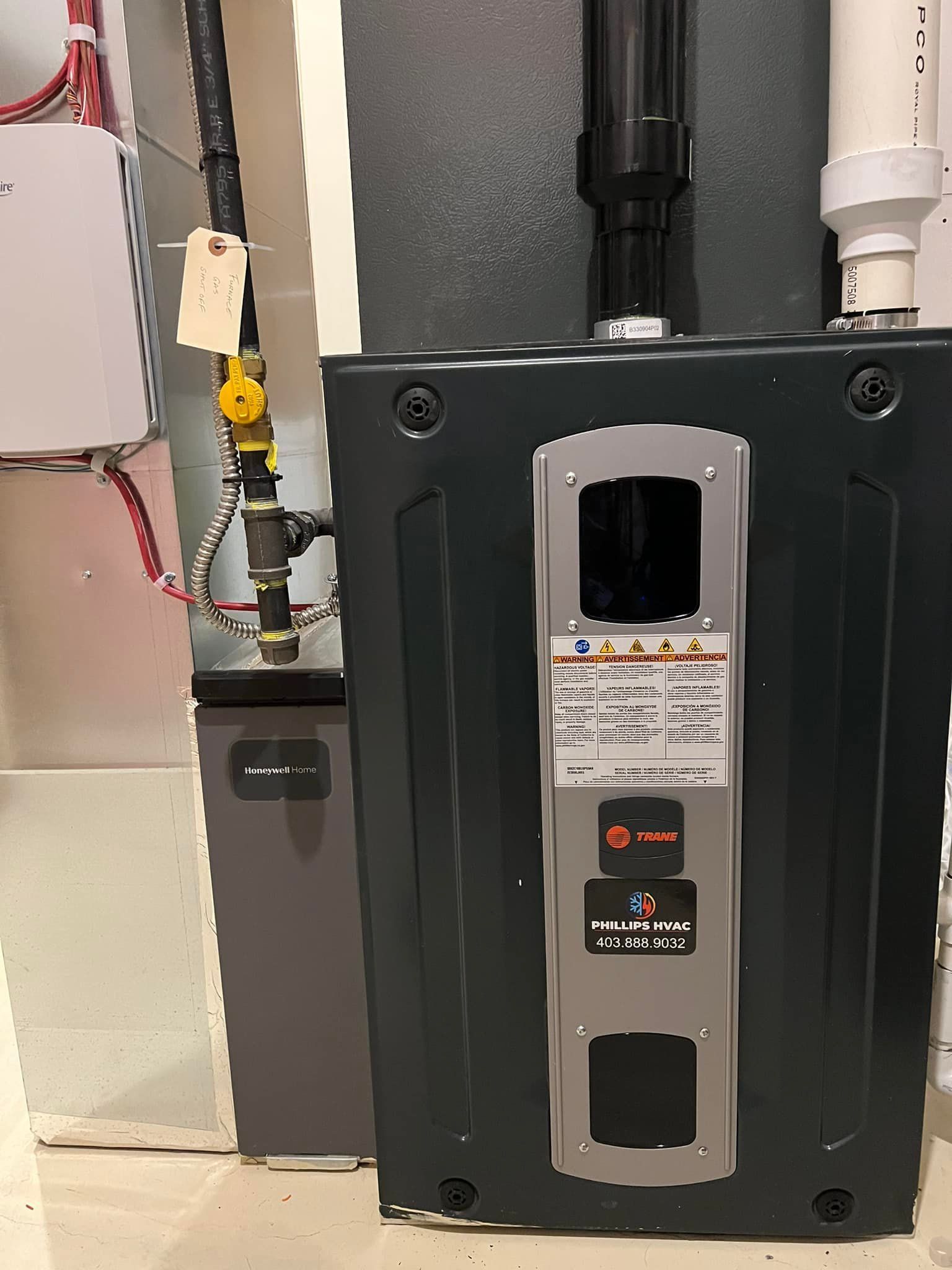 Dark gray furnace with black pipe and yellow gas line; indoor setting.