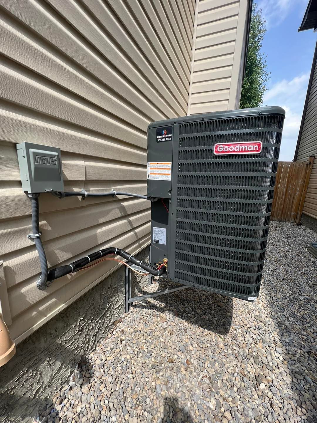 Outdoor HVAC unit against a beige siding wall, with electrical box and pipes, on gravel.