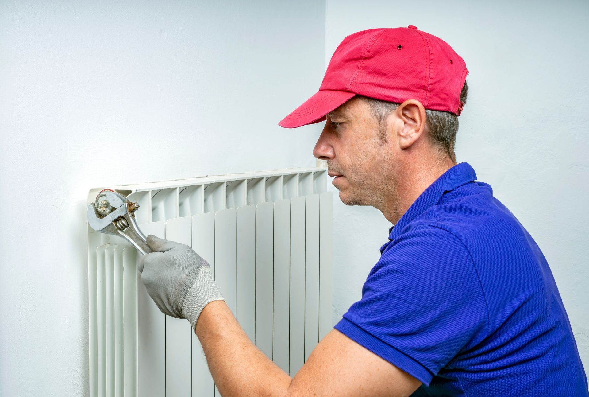 A man is fixing a radiator with a wrench.