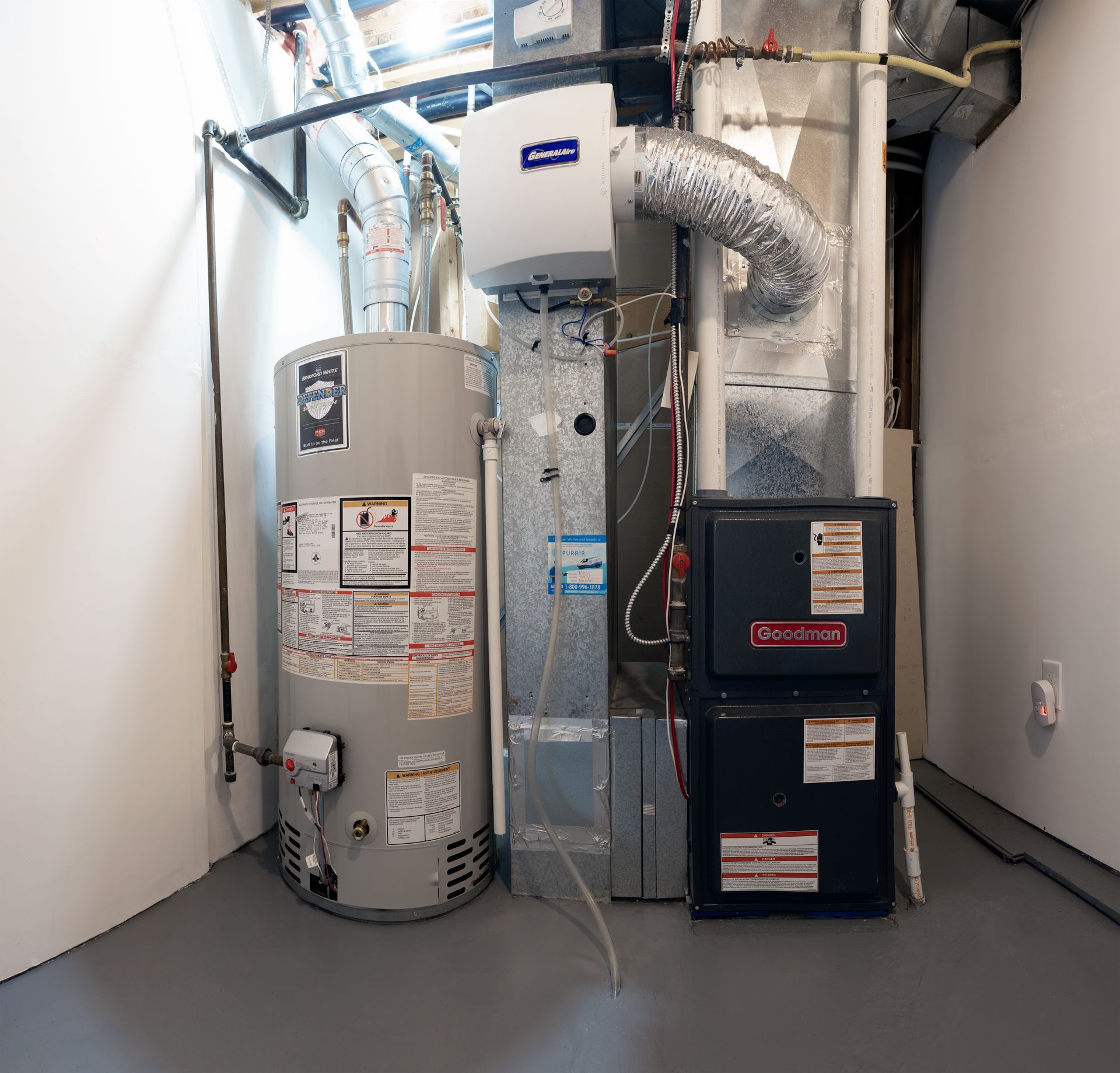 Water heater, furnace, and humidifier in a utility room. Gray appliances on a gray floor against white walls.