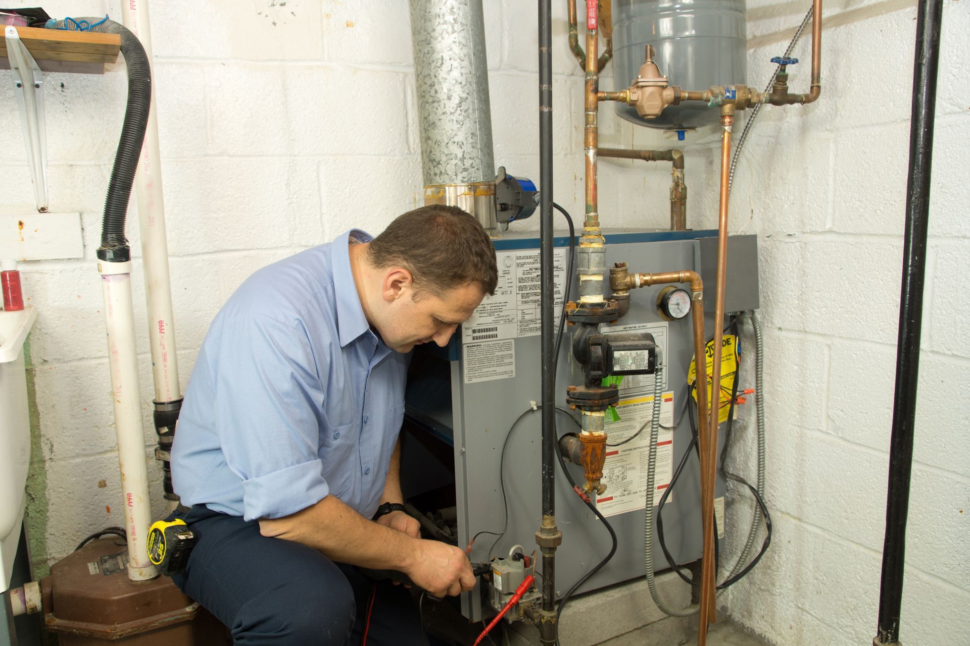 A man is working on a heating system in a basement.