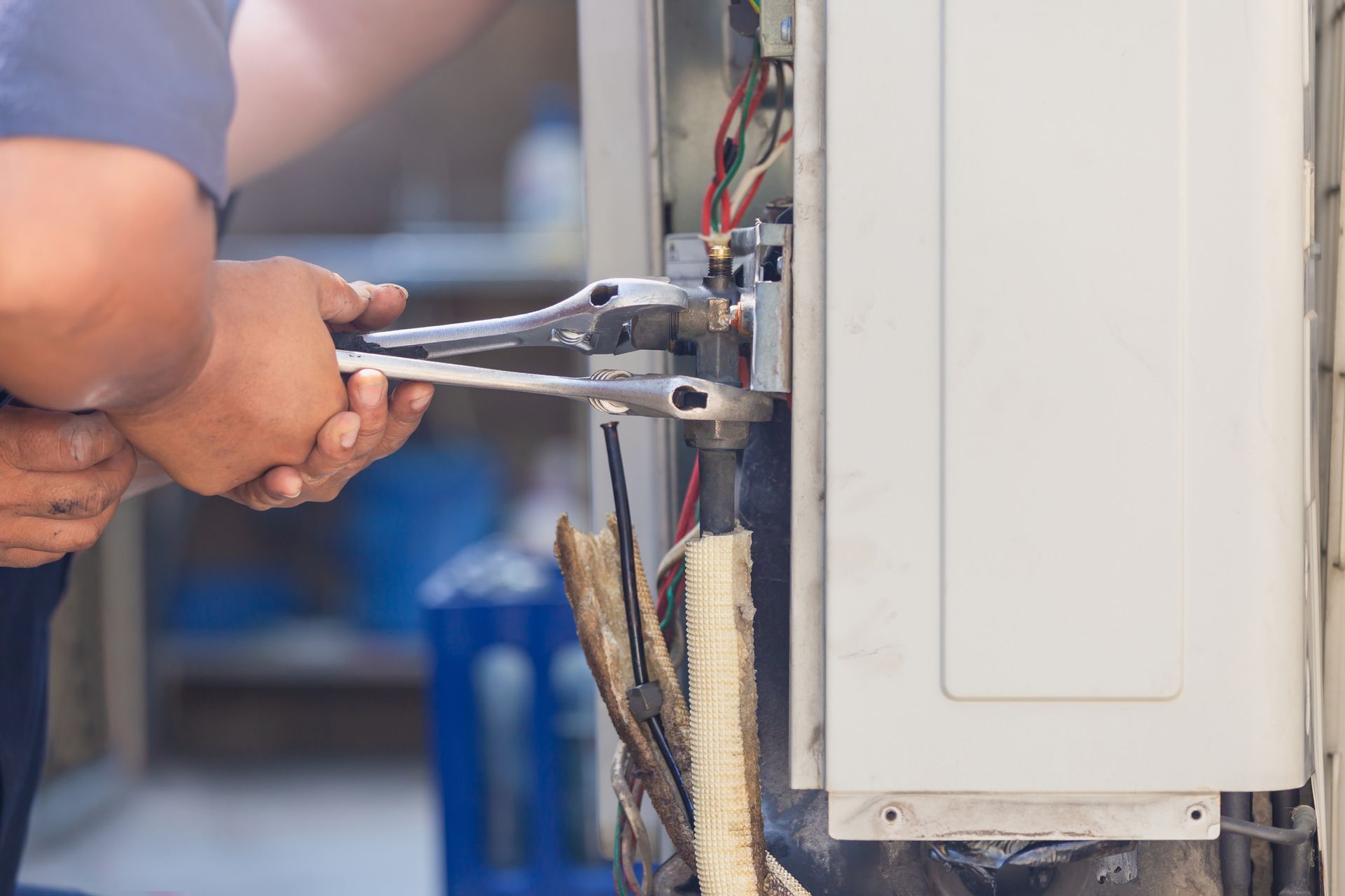 A man is fixing an air conditioner with a wrench.