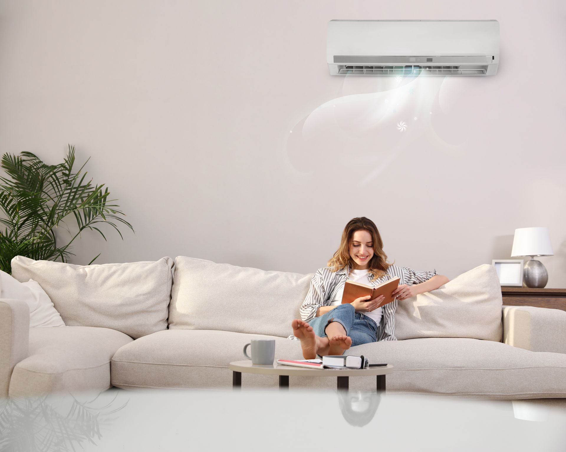 A woman is sitting on a couch reading a book under an air conditioner.