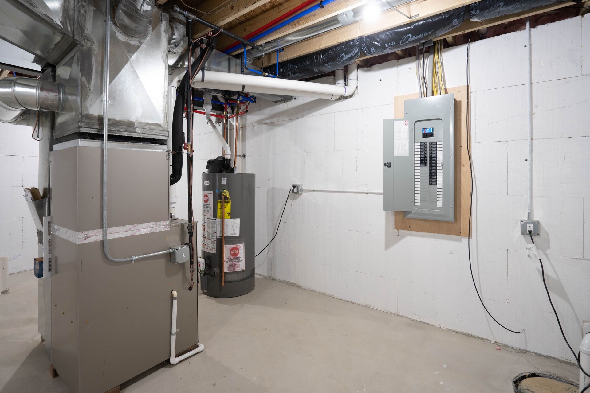 A basement with a furnace , water heater , and electrical panel.