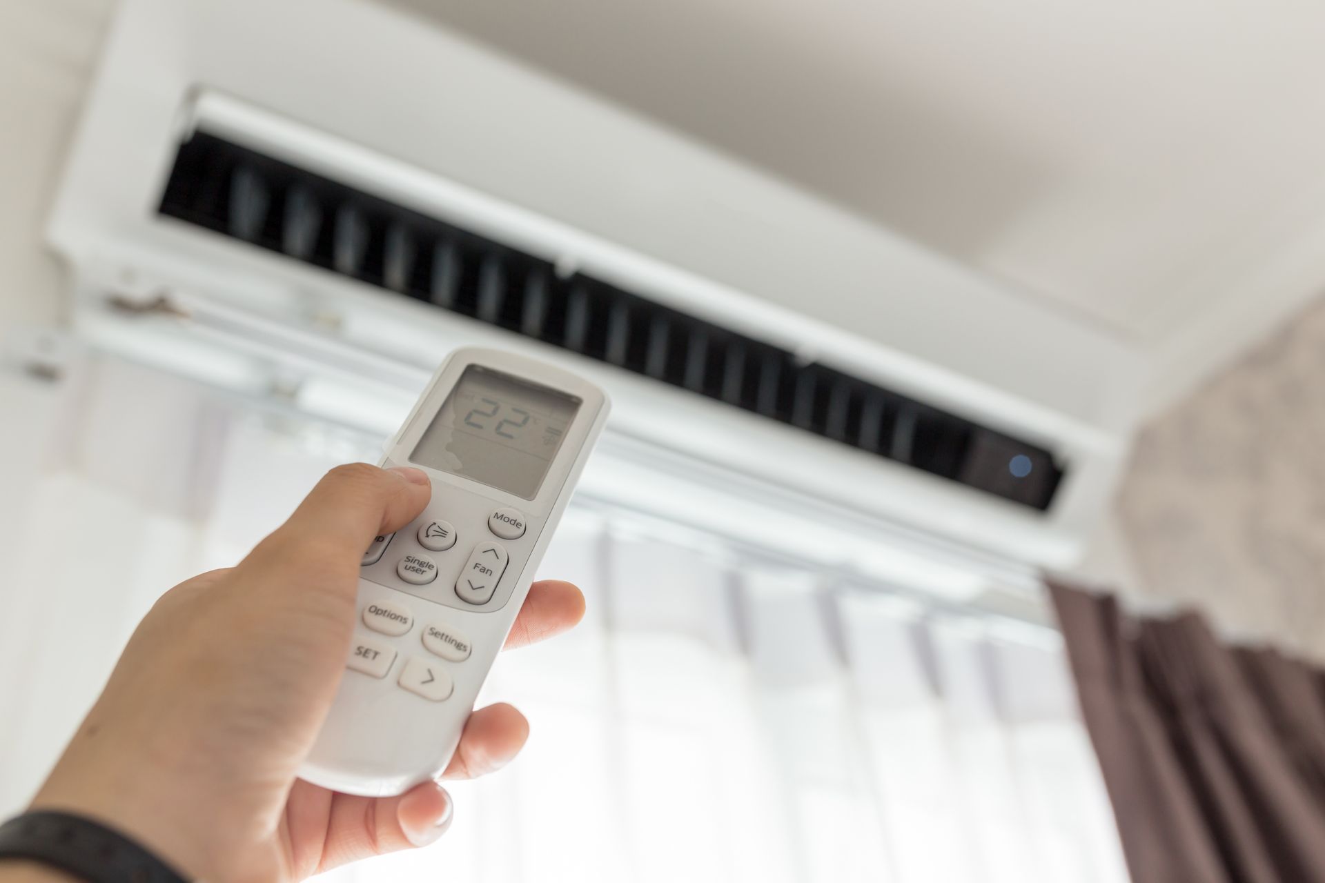 A person is holding a remote control in front of an air conditioner.