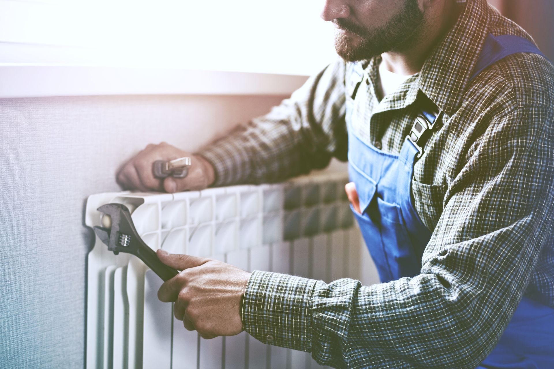 A man is fixing a radiator with a wrench.