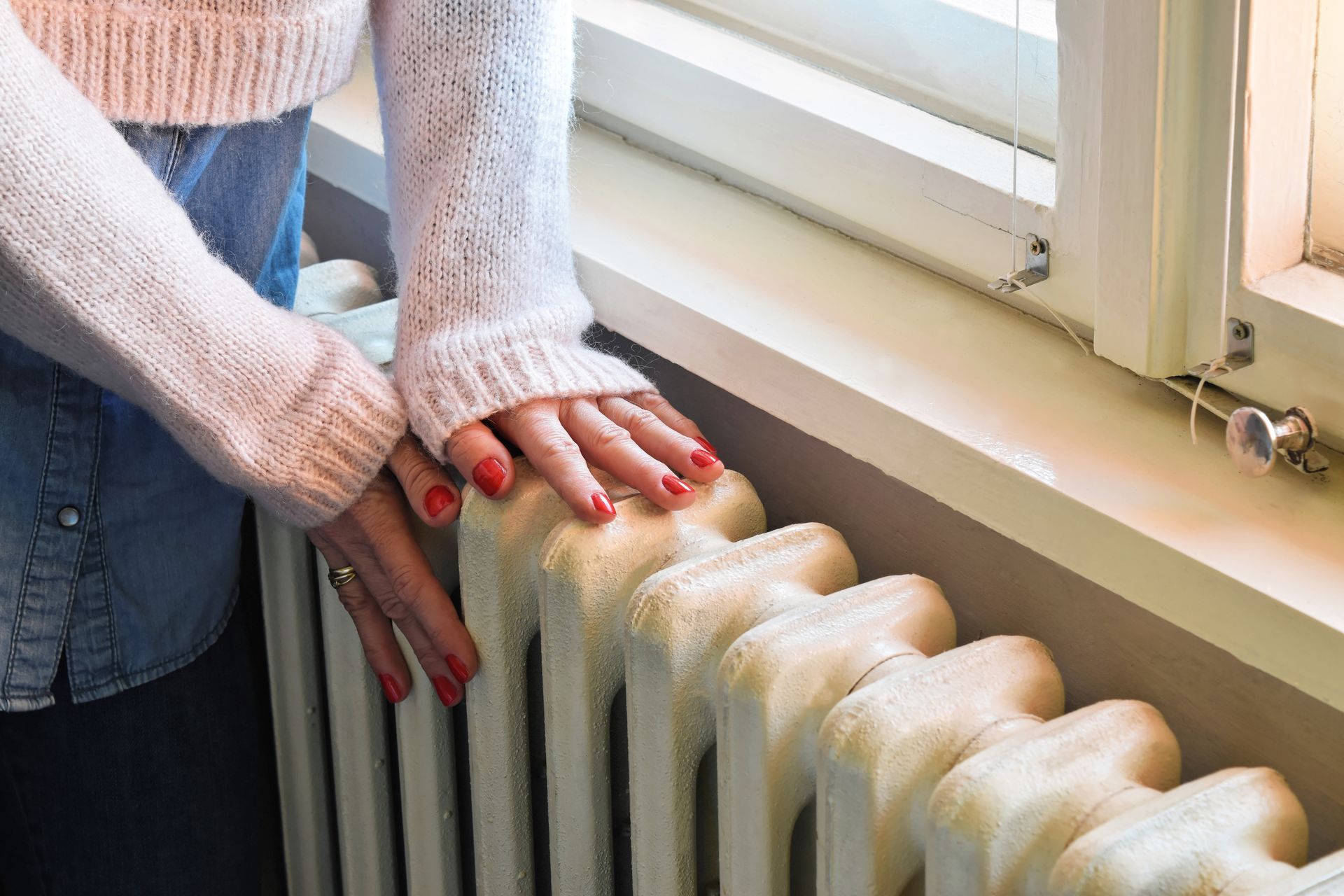 A woman is standing next to a radiator in front of a window.