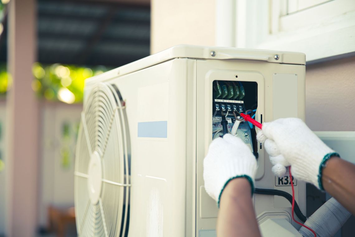 A person is working on an air conditioner with a voltmeter.