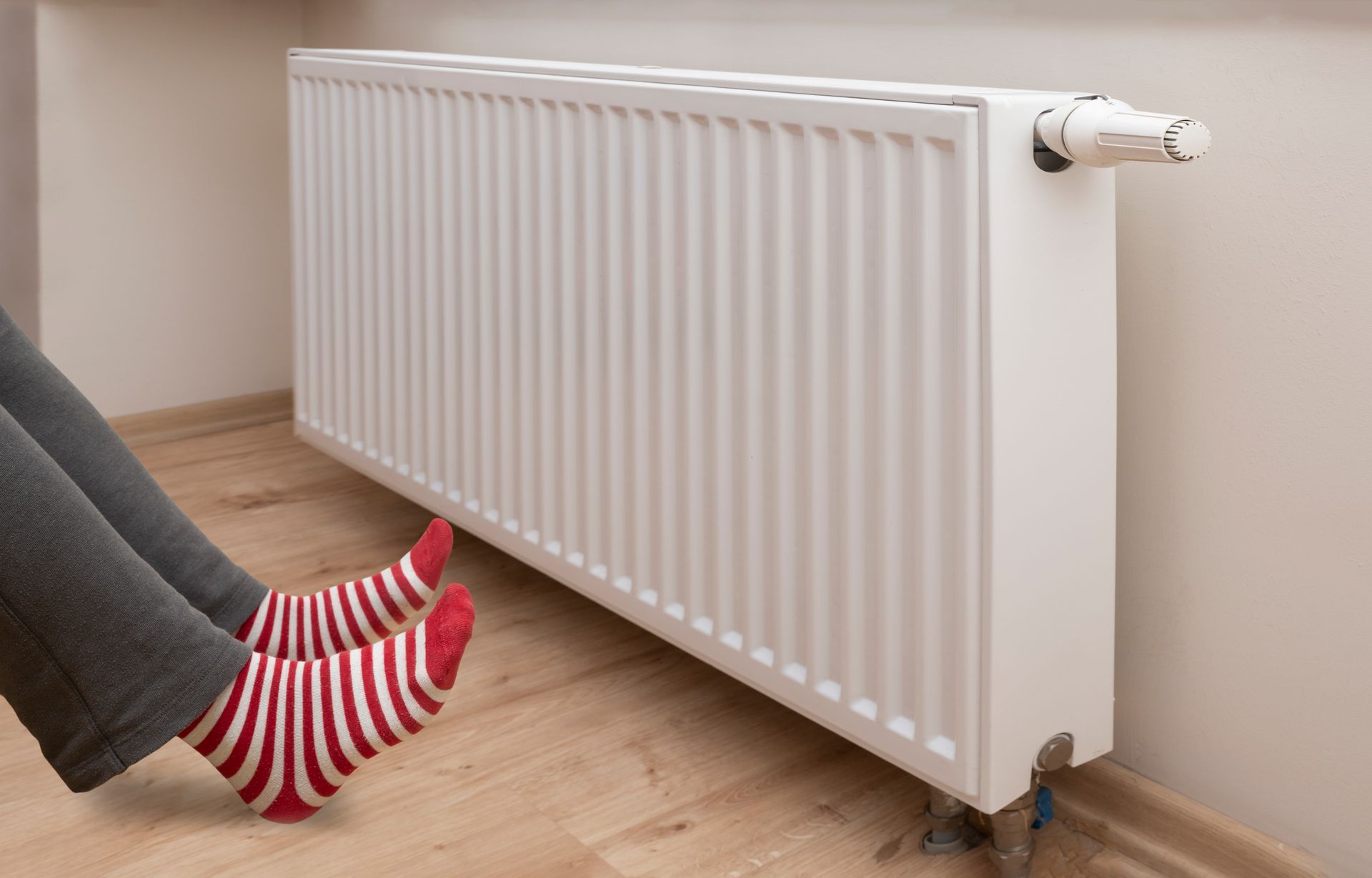 A person wearing red and white striped socks is sitting on the floor next to a radiator.