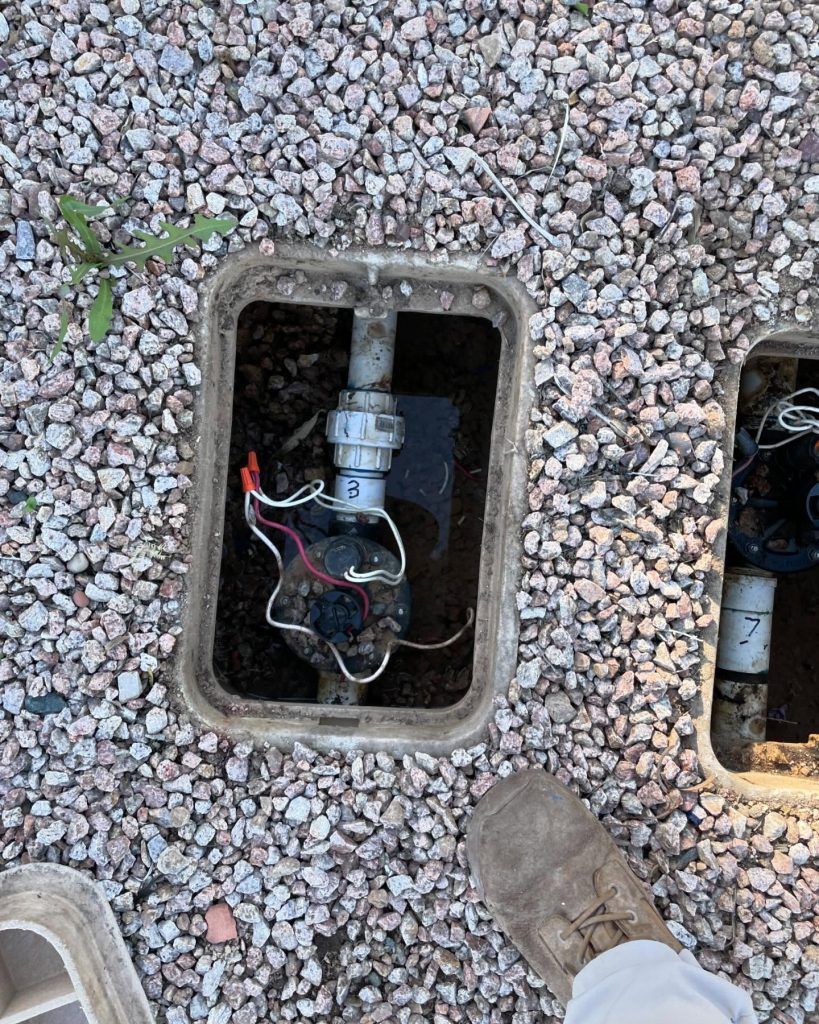 Sprinkler valve in a gravel box, with electrical wiring.