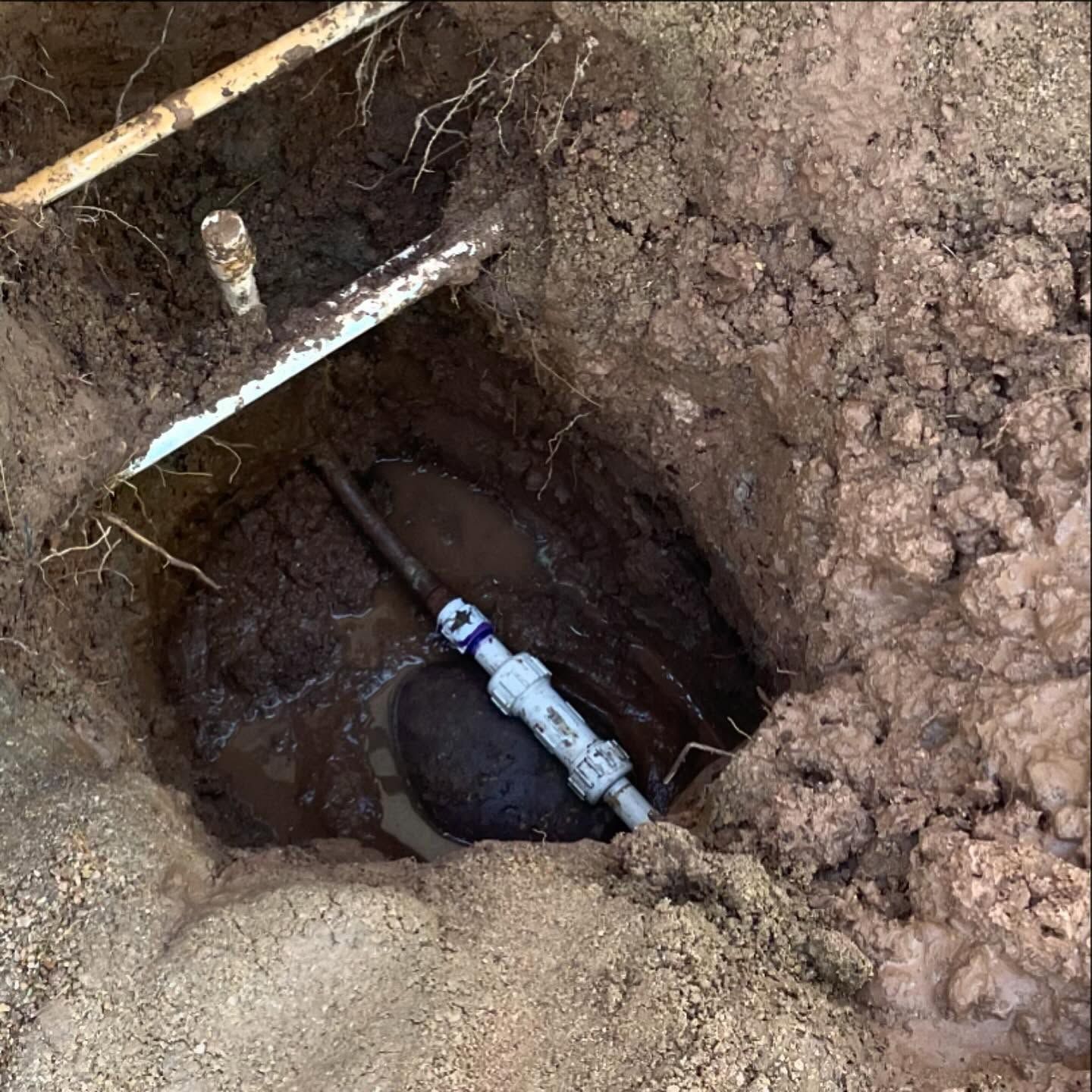 Hole in the ground revealing a broken water pipe; mud and standing water.
