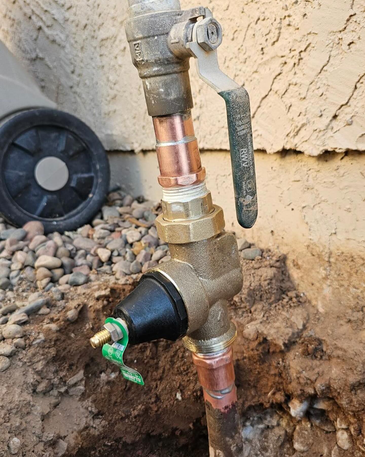 Outdoor plumbing, bronze and copper water valve with a black and green component.