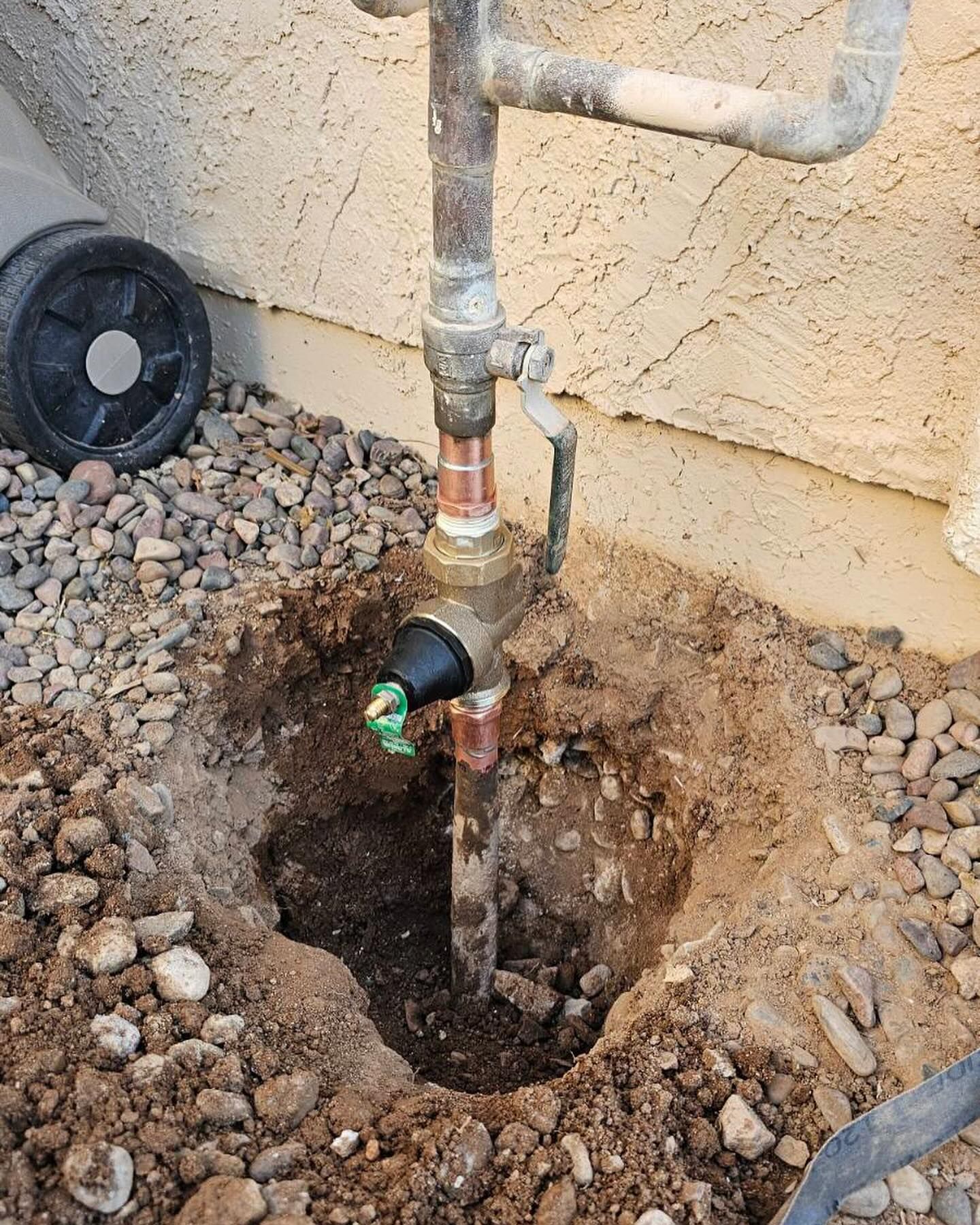A small hole dug in gravel surrounds a sprinkler system valve connected to copper pipes.