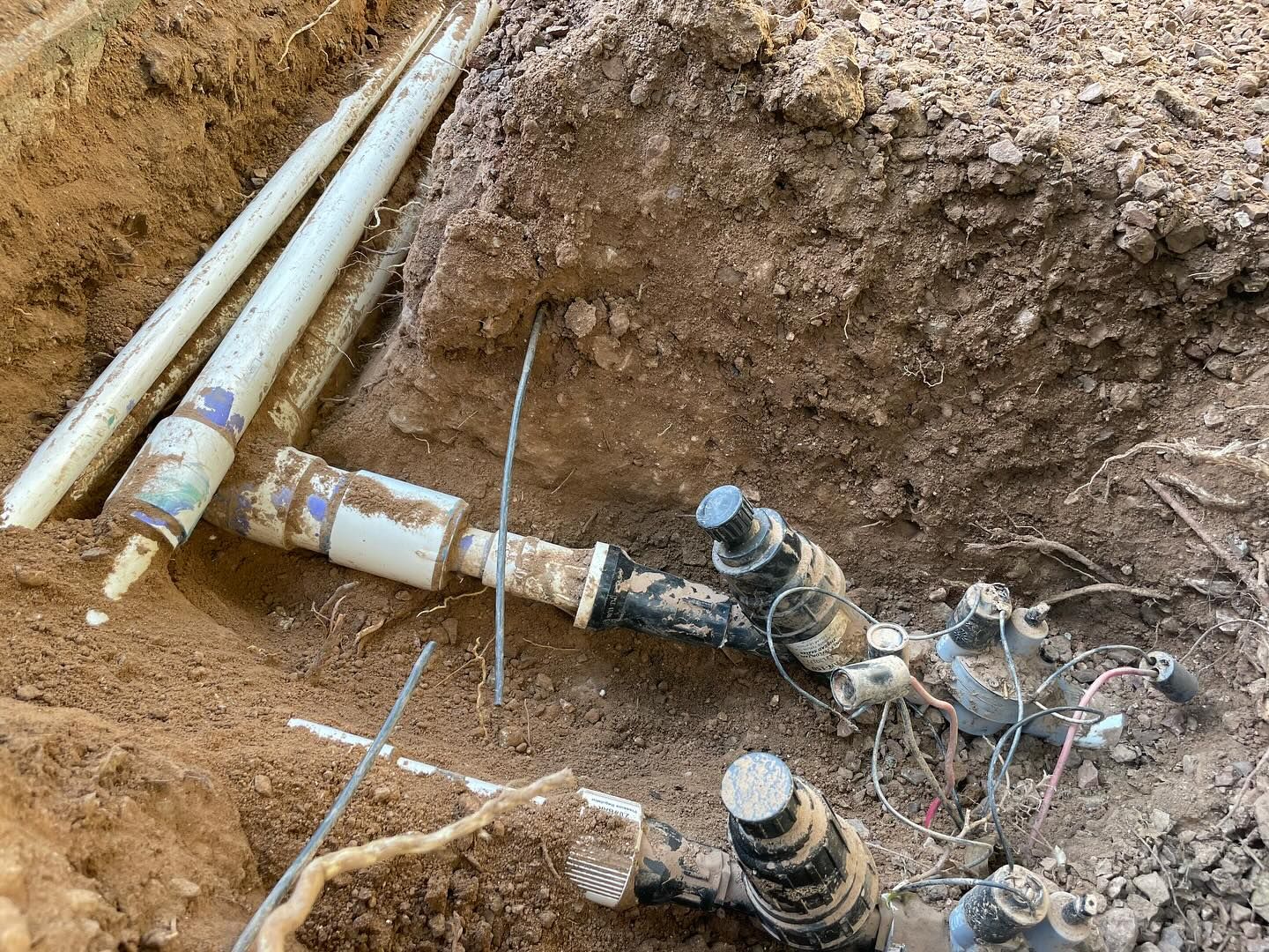 Excavation of irrigation system components in dirt, showing pipes, valves, and wiring.