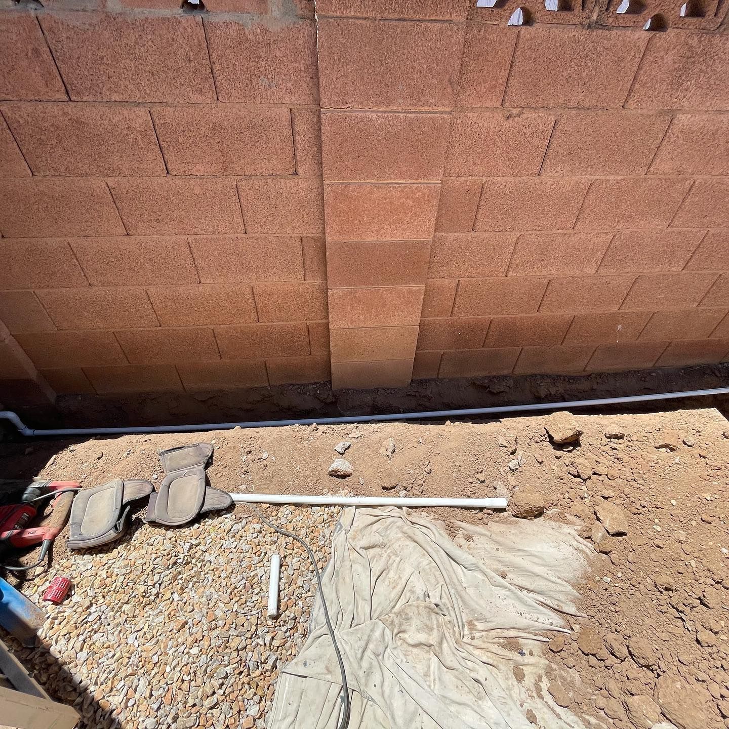 Construction site with red brick wall, dirt, gravel, and white pipes.