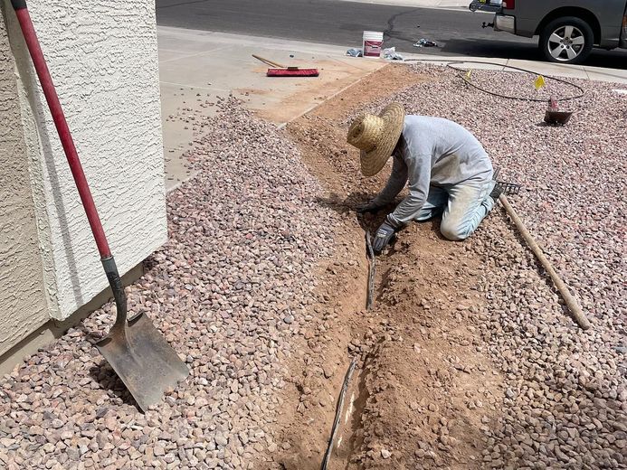Person kneeling in a trench, working on a landscaping project in a rocky yard.