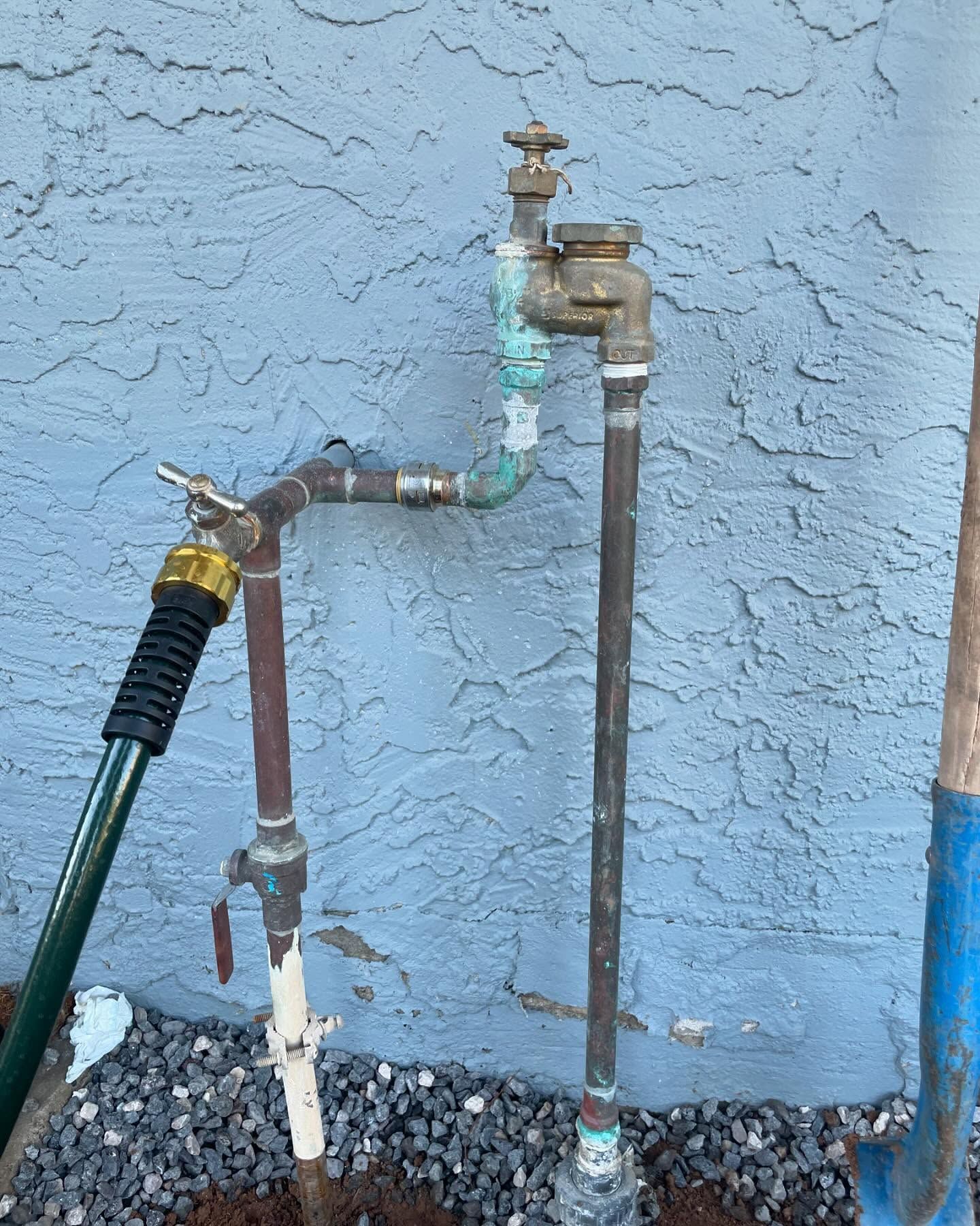 Outdoor water faucet with hose attached, against a blue stucco wall.