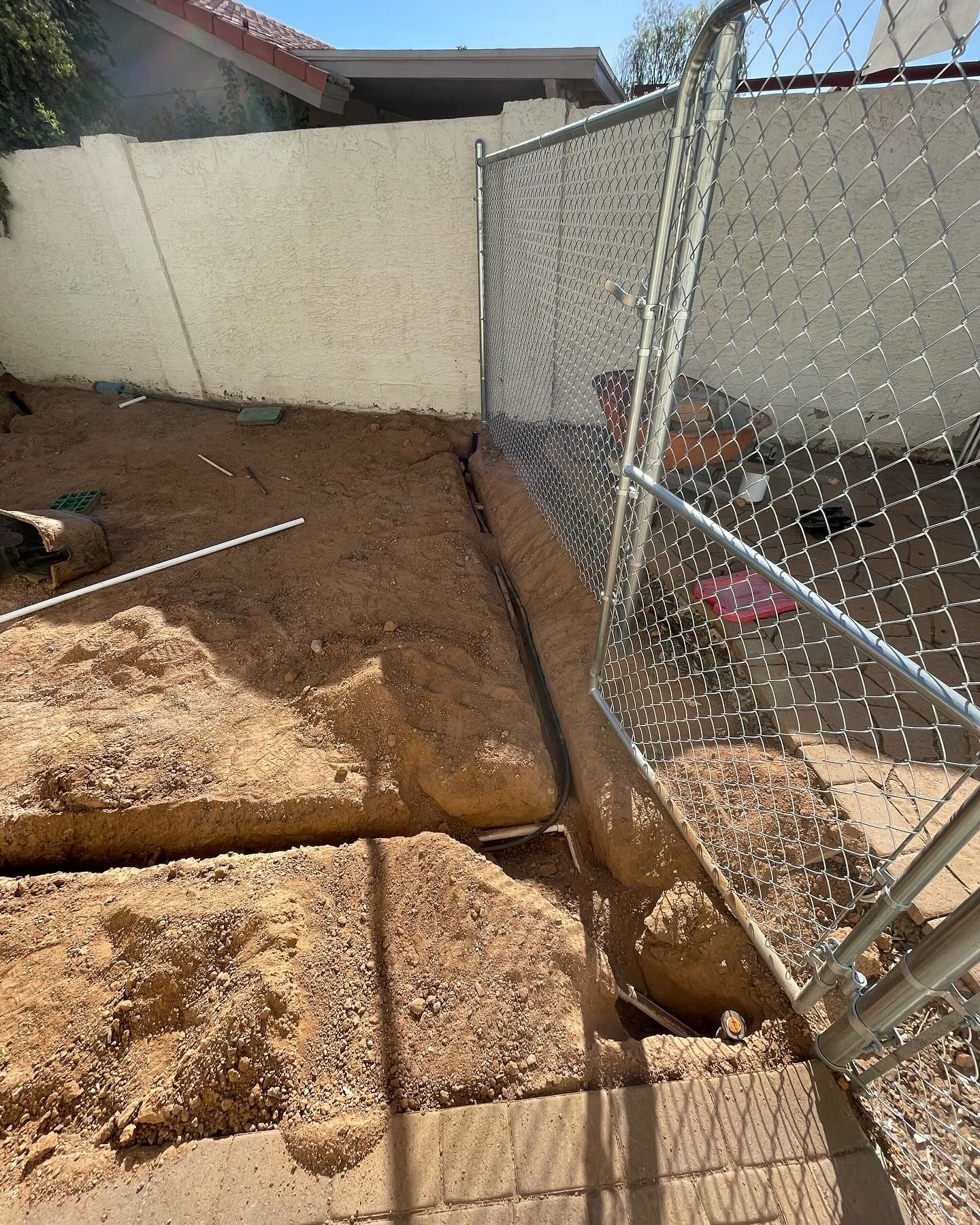 A dirt trench along a chain-link fence and wall. Sand piles, with a partly open gate.