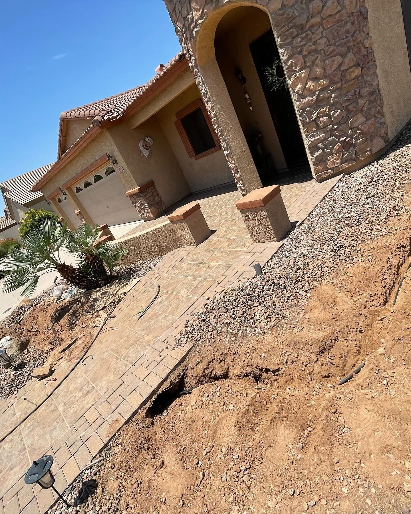 A brick walkway leading to a house with a stone facade. The walkway slopes downhill and is under construction.