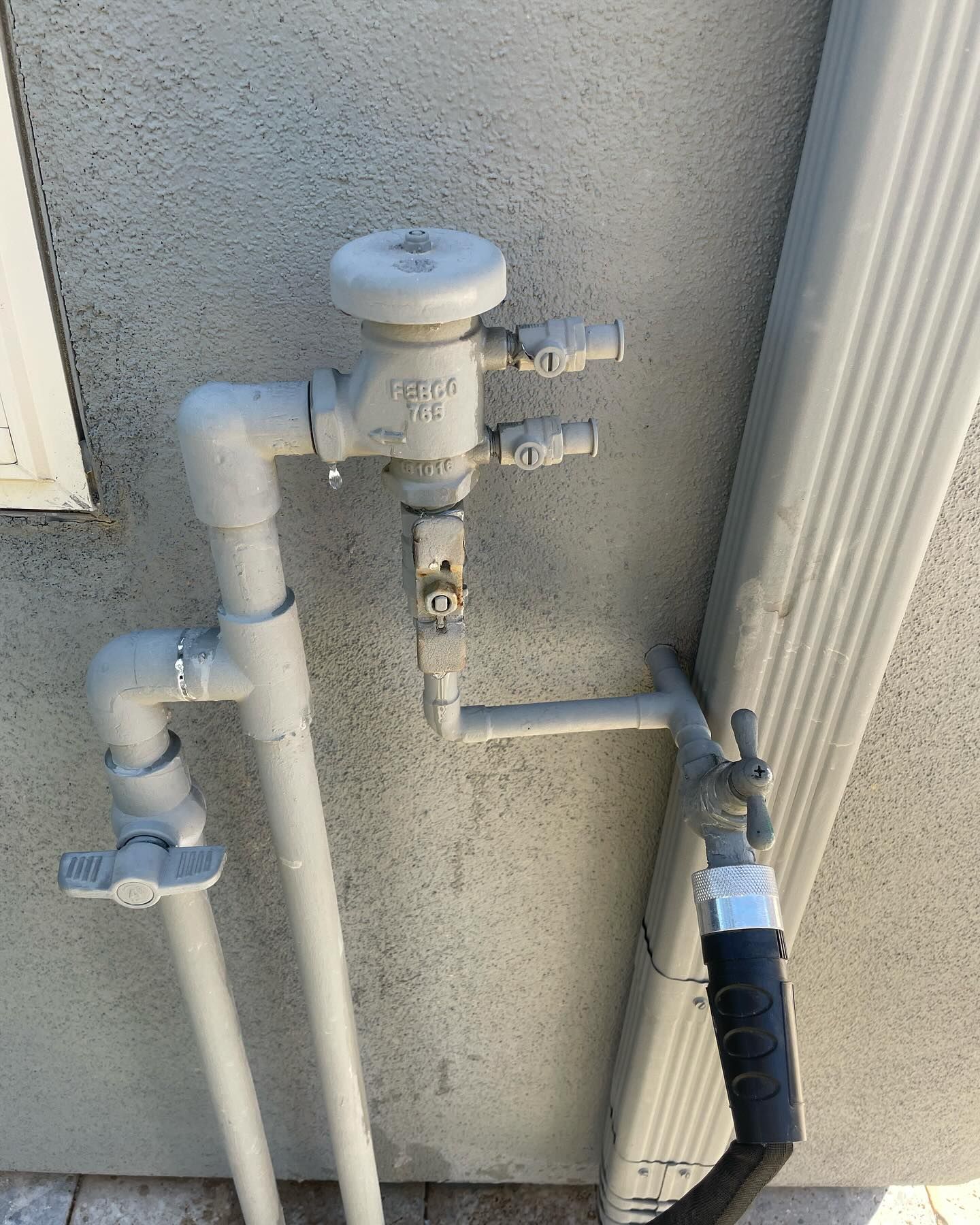 Gray irrigation system pipes and valves against a stucco wall, connected to a gutter.