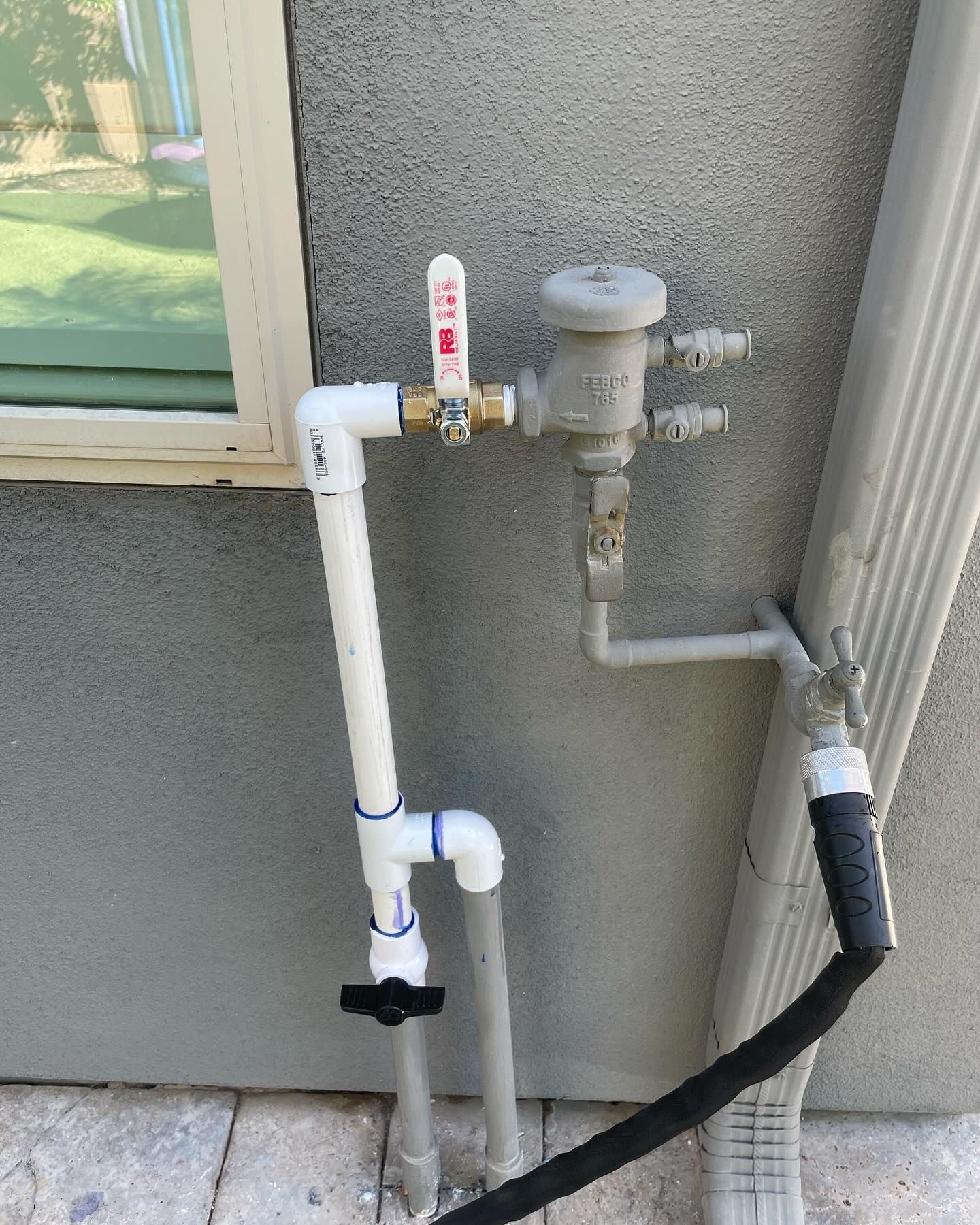 Pipes and valves attached to a wall, with a hose connected, likely for outdoor water access.