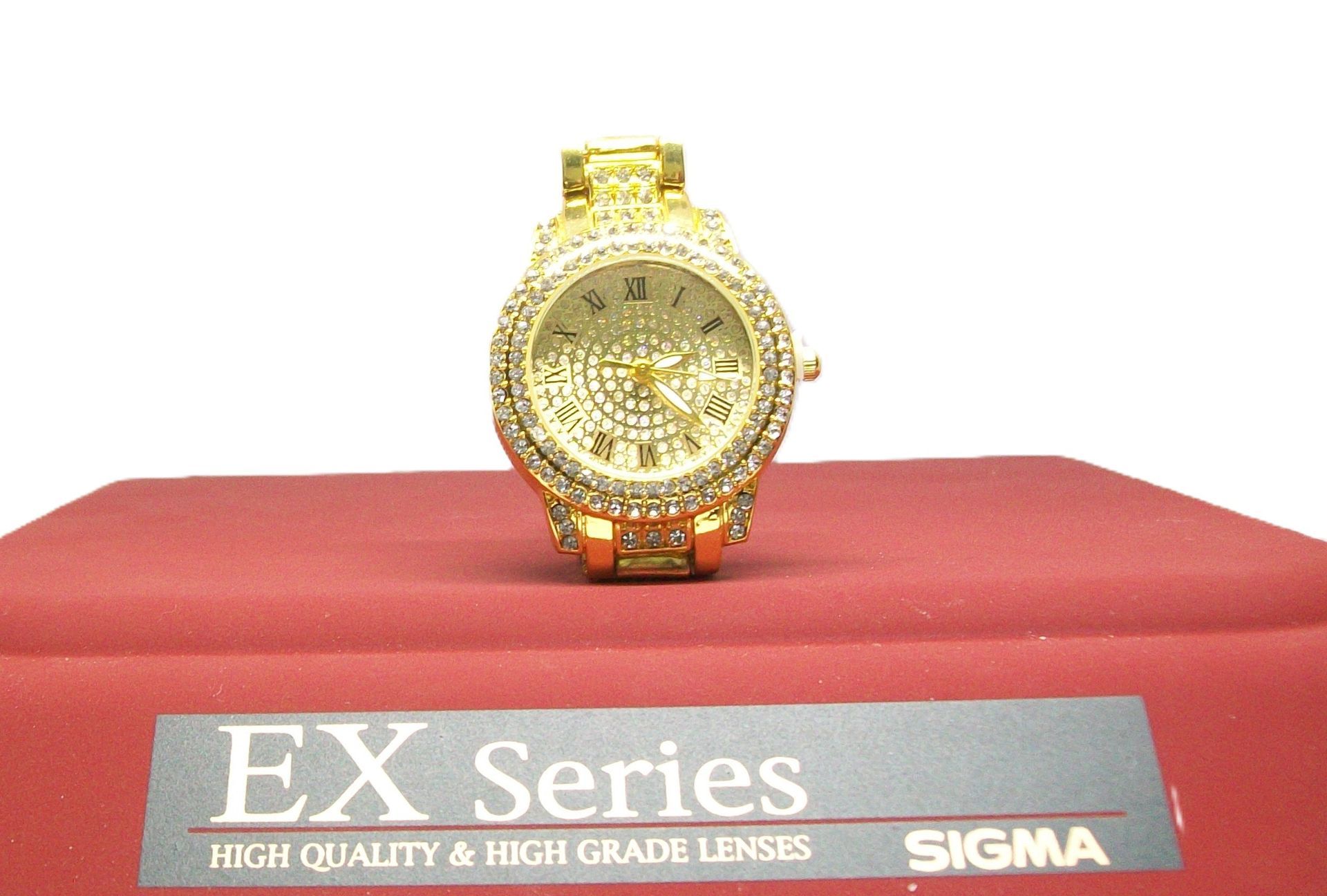 Gouden, met diamanten bezette polshorloge op een rood oppervlak met zichtbare "EX Series"- en "SIGMA"-branding.