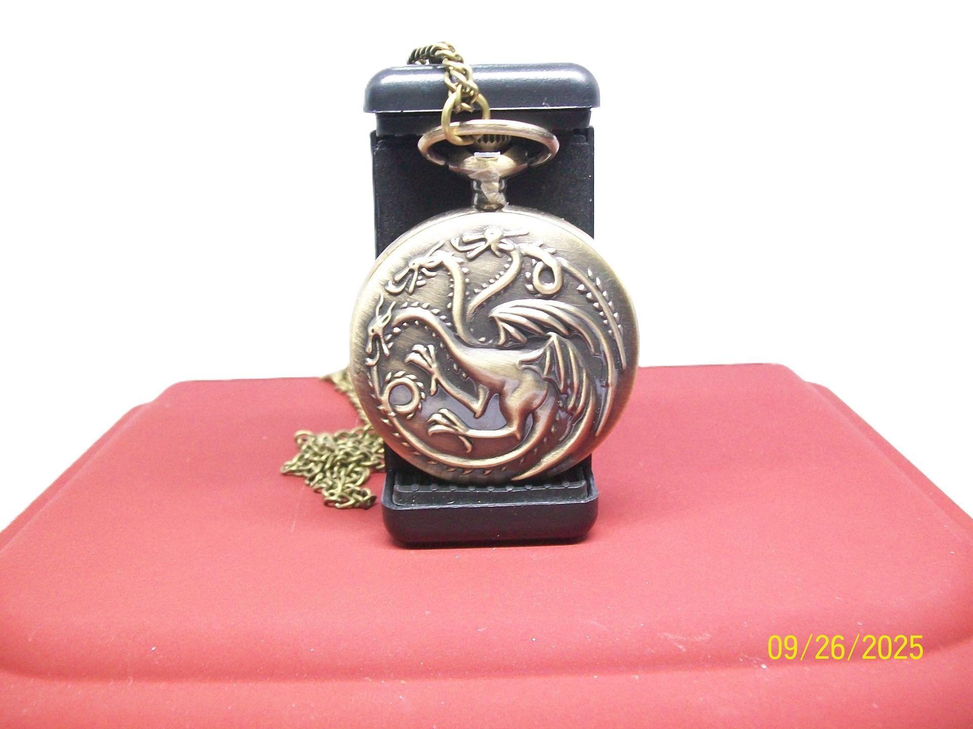 Zakhorloge, goudkleurig, op een zwarte standaard, opengevouwen zodat de witte wijzerplaat en de tijd zichtbaar zijn.