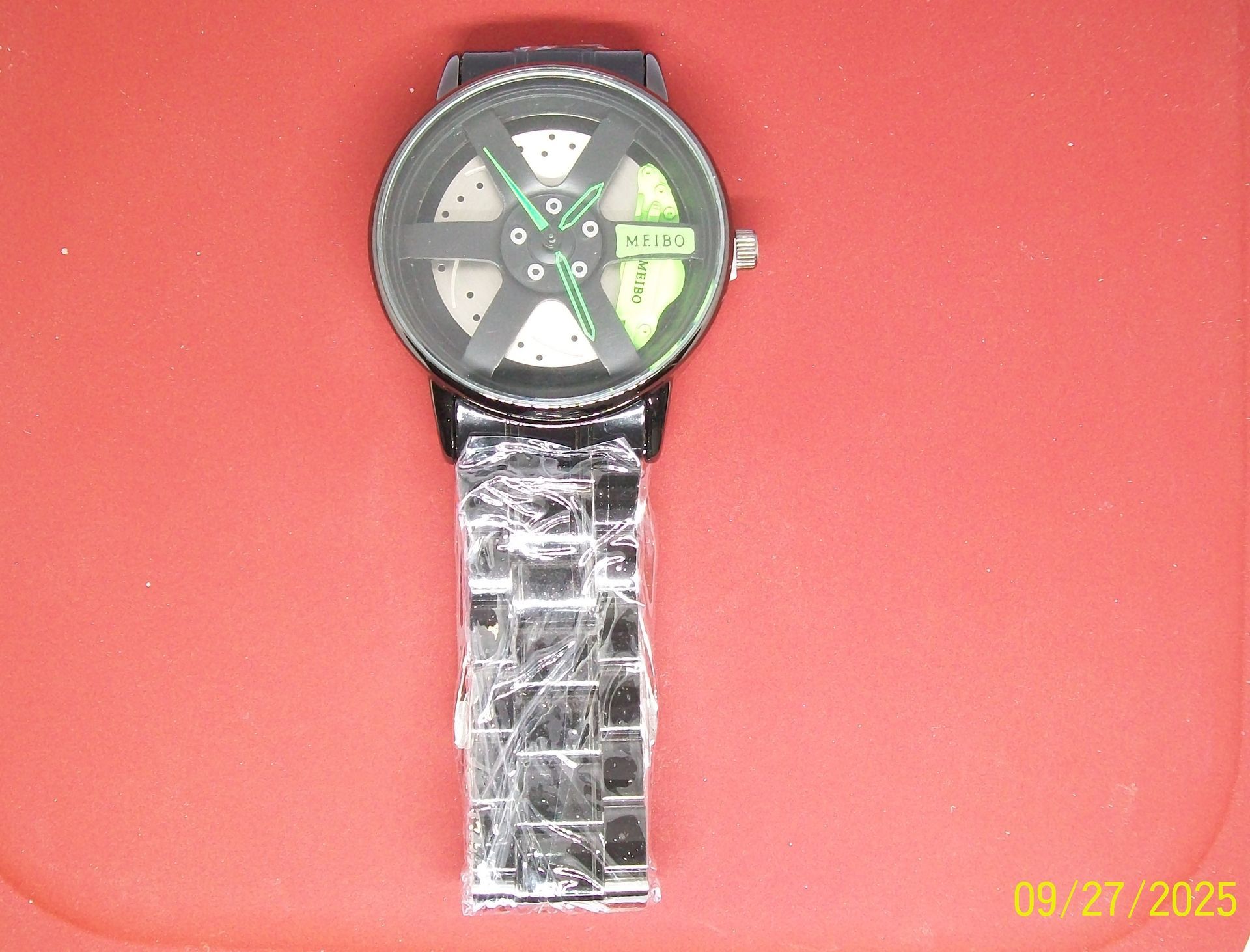 Een polshorloge met een autowielontwerp, zwarte en groene accenten, geïsoleerd op een witte achtergrond.