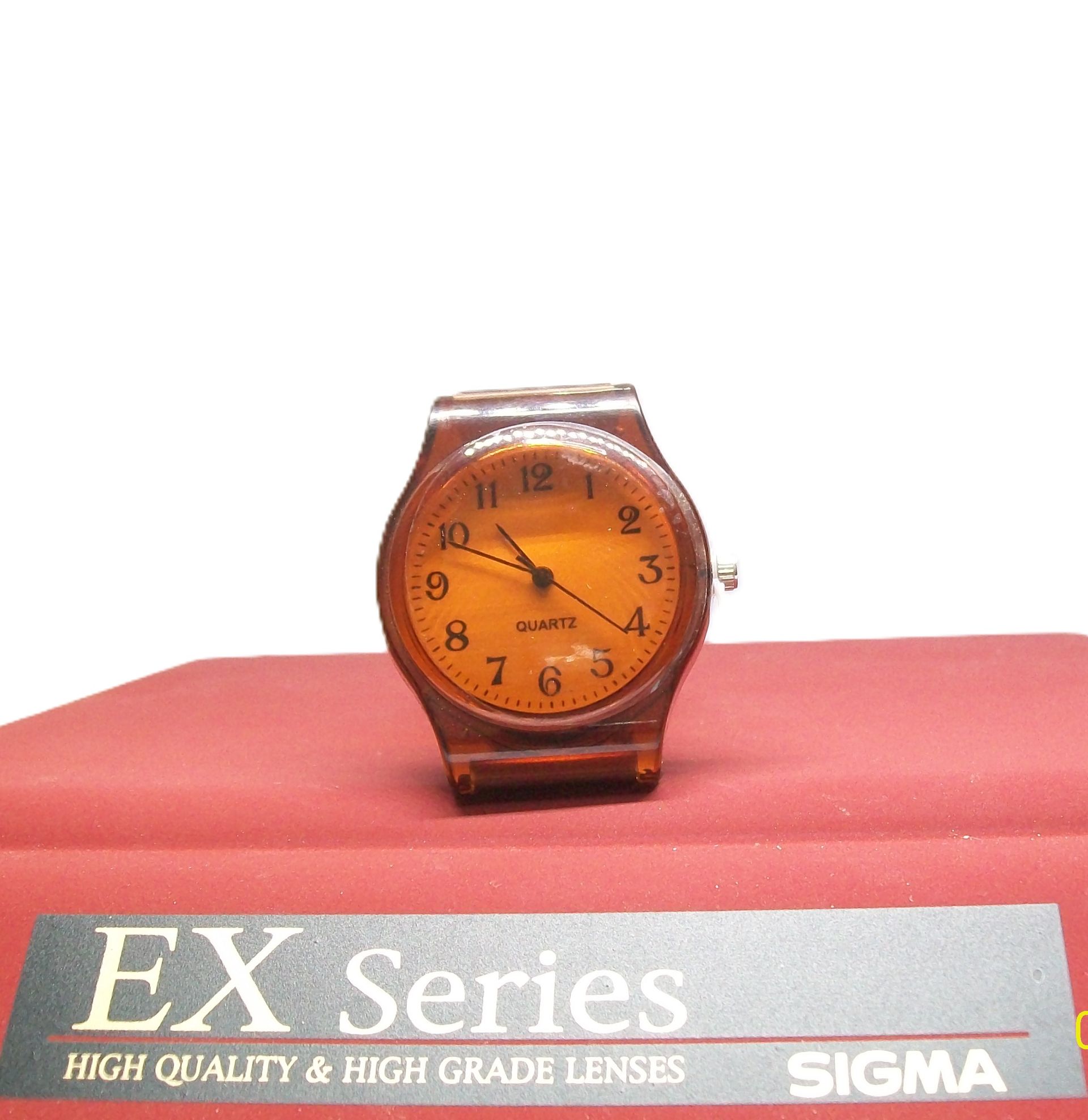 Oranjekleurig polshorloge op een rood oppervlak met de tekst "EX Series" en het merk "SIGMA" aan de onderkant.