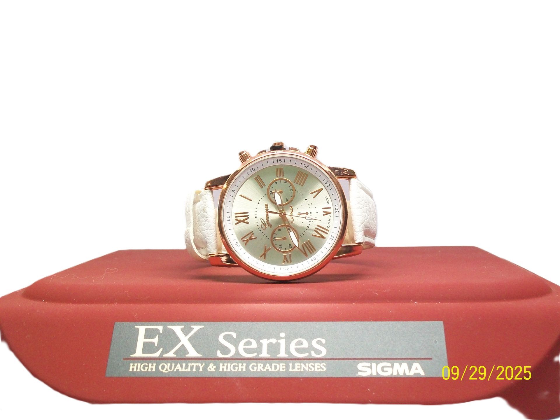 Gouden horloge met een lichtgroene wijzerplaat op een rode standaard, tegen een witte achtergrond.