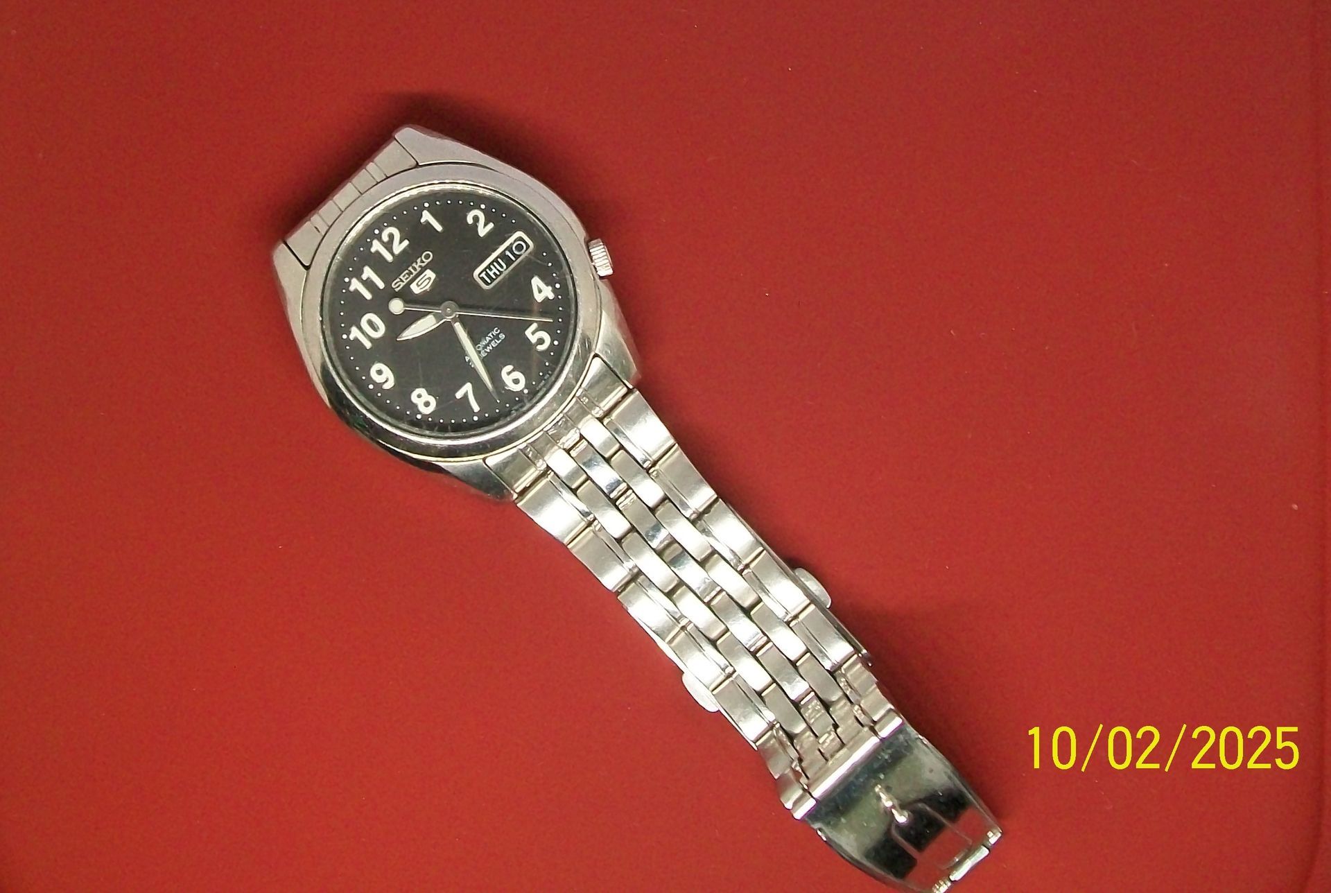 Zilveren polshorloge met zwarte wijzerplaat op rood platform, 