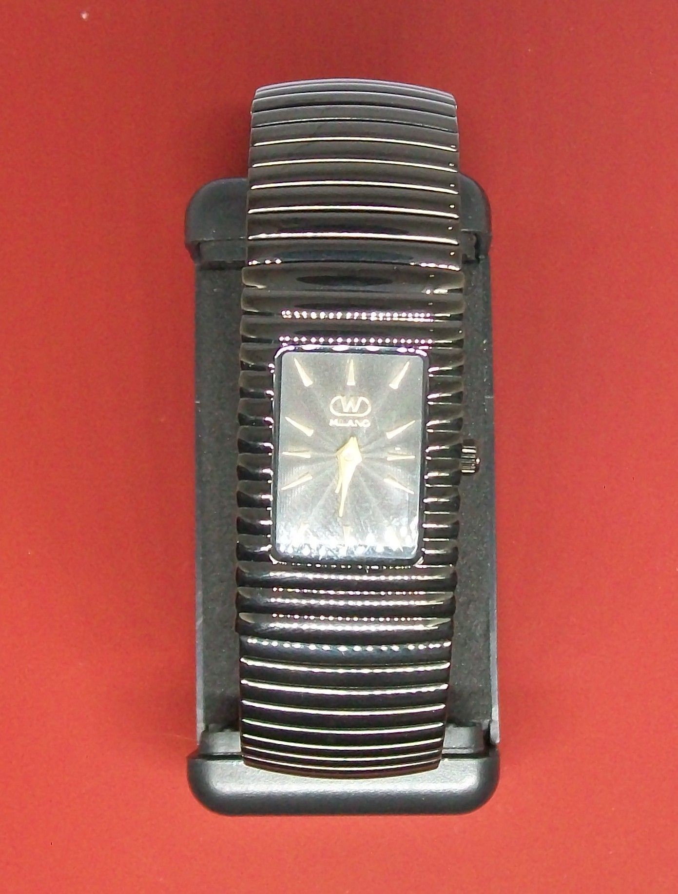 Zwart horloge op een zwarte standaard, zittend op een rood oppervlak, Sigma-lenstekst.