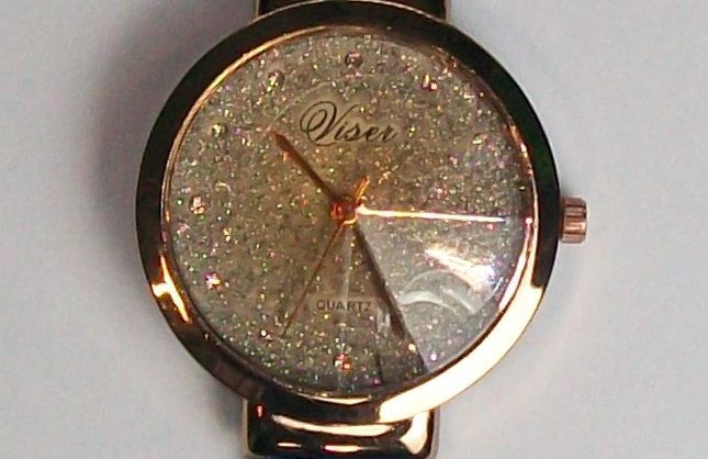 Horloge met blauwe band, goudkleurige kast en glinsterende wijzerplaat op een wit oppervlak.