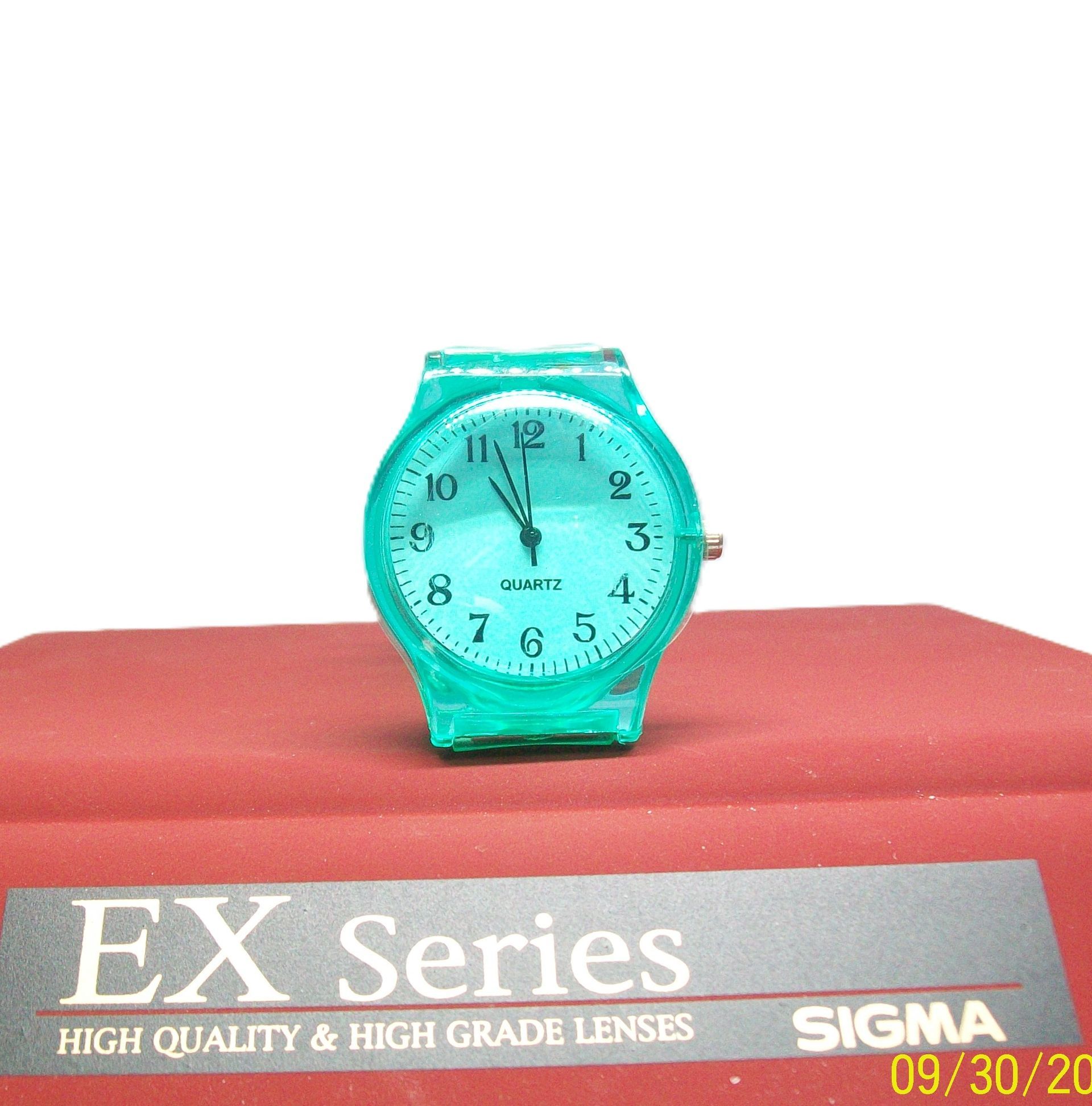 Groen quartzhorloge op een rood oppervlak, met daaronder de tekst "EX Series" en "SIGMA".