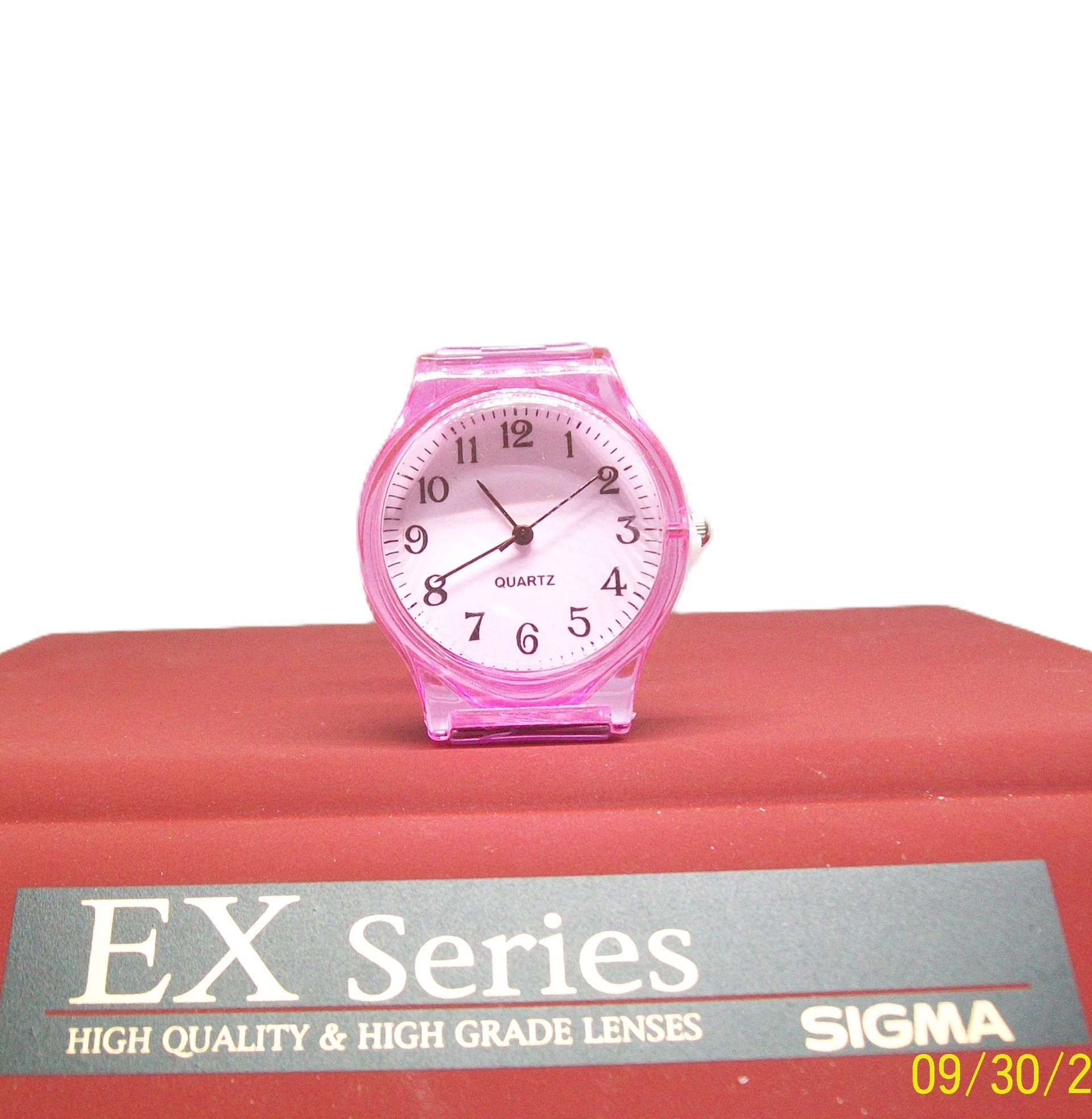 Roze Timex-horloge op een rood oppervlak, met een Sigma-lensadvertentie op de voorgrond.