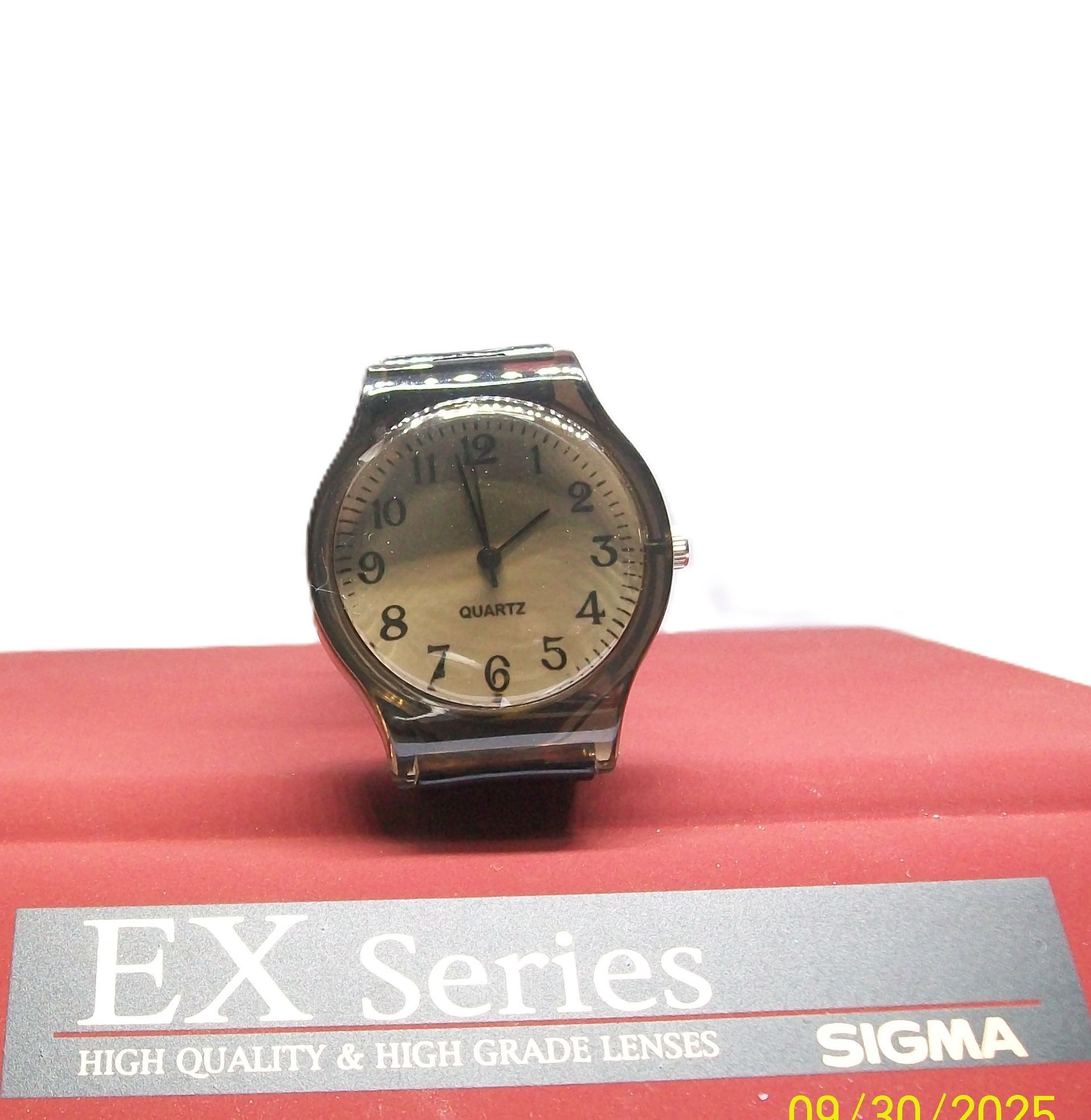 Een zilveren horloge met een beige wijzerplaat ligt op een rood oppervlak. De tekst bevat "EX Series" en "SIGMA".
