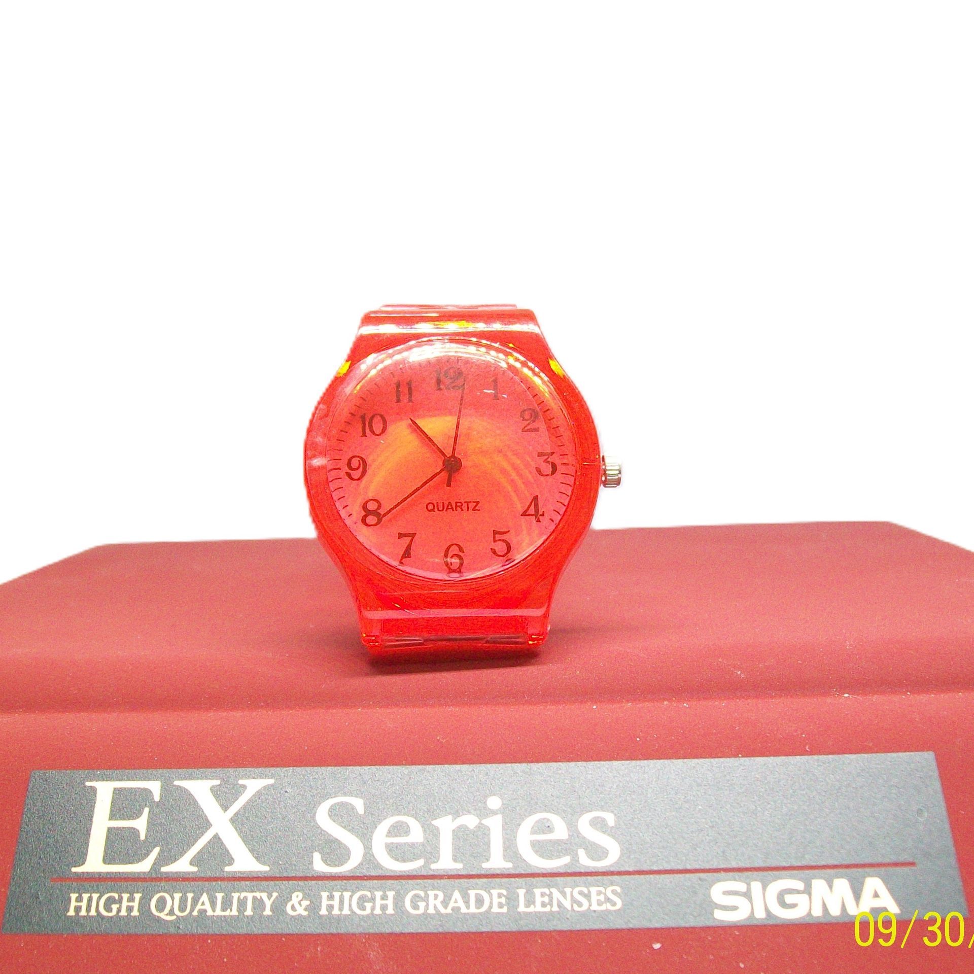 Rood Timex horloge op een rood oppervlak met "EX Series" label, cijfers op de wijzerplaat.