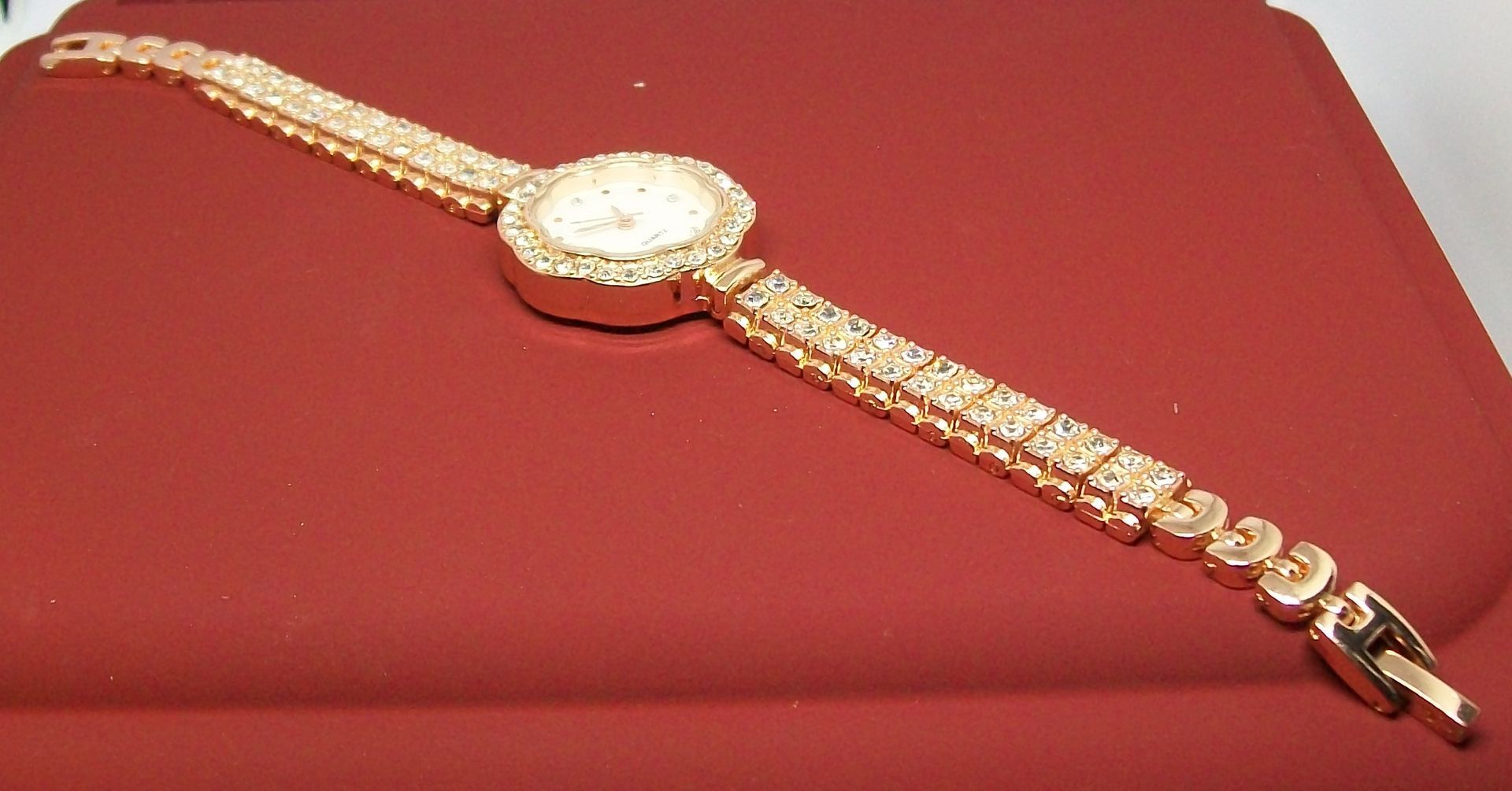 Gouden horloge met kristallen versieringen op een rood oppervlak. De tekst