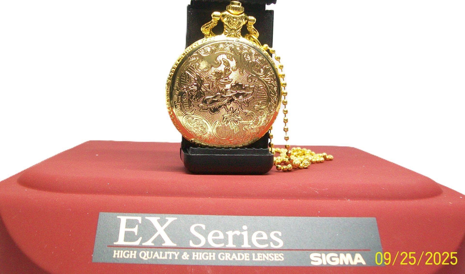 Gouden zakhorloge op een rood oppervlak, ketting zichtbaar. 