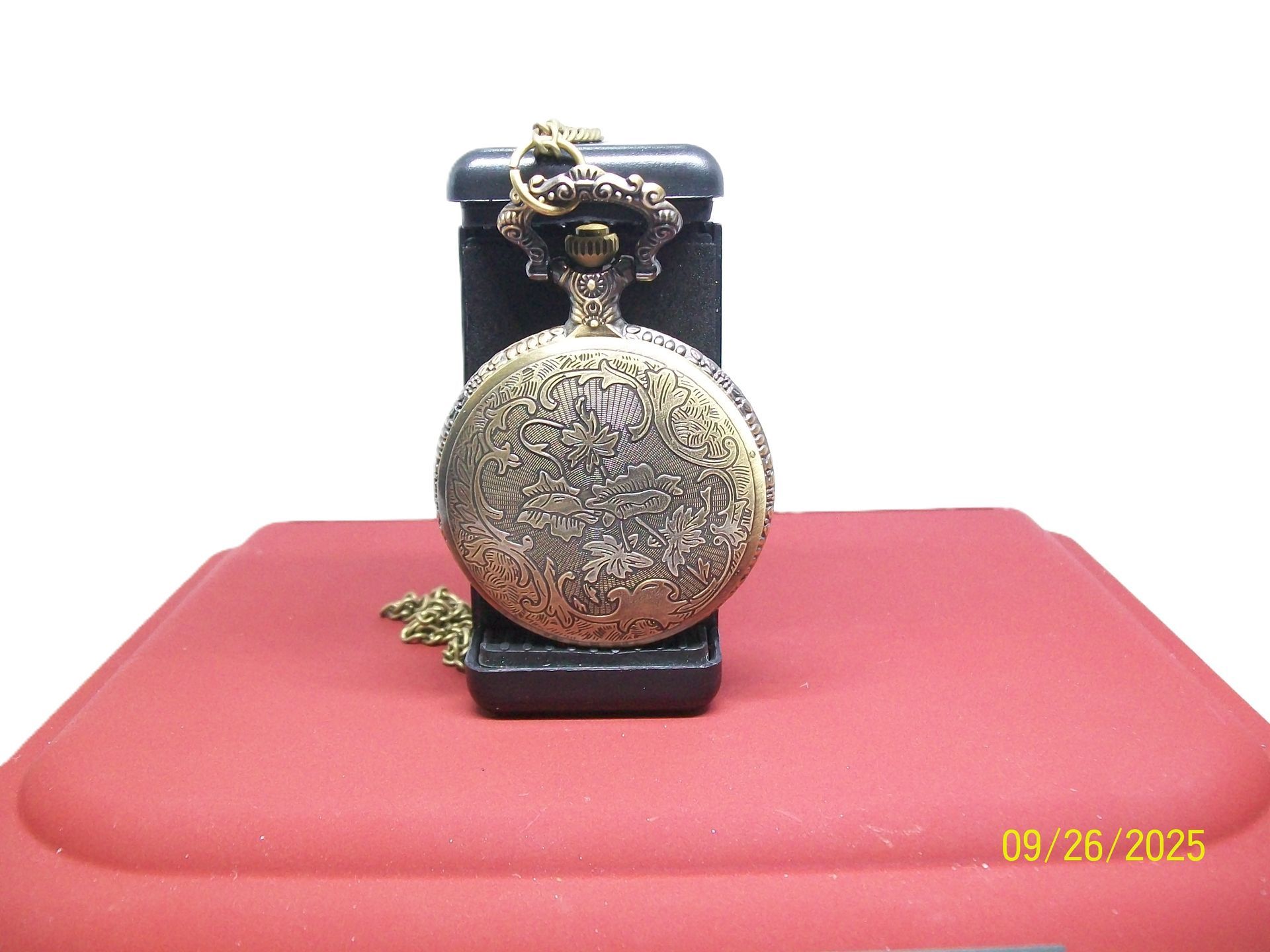 Zakhorloge op een rood oppervlak met open deksel, waarop de tijd staat aangegeven. Daarachter zit een zwarte kast.