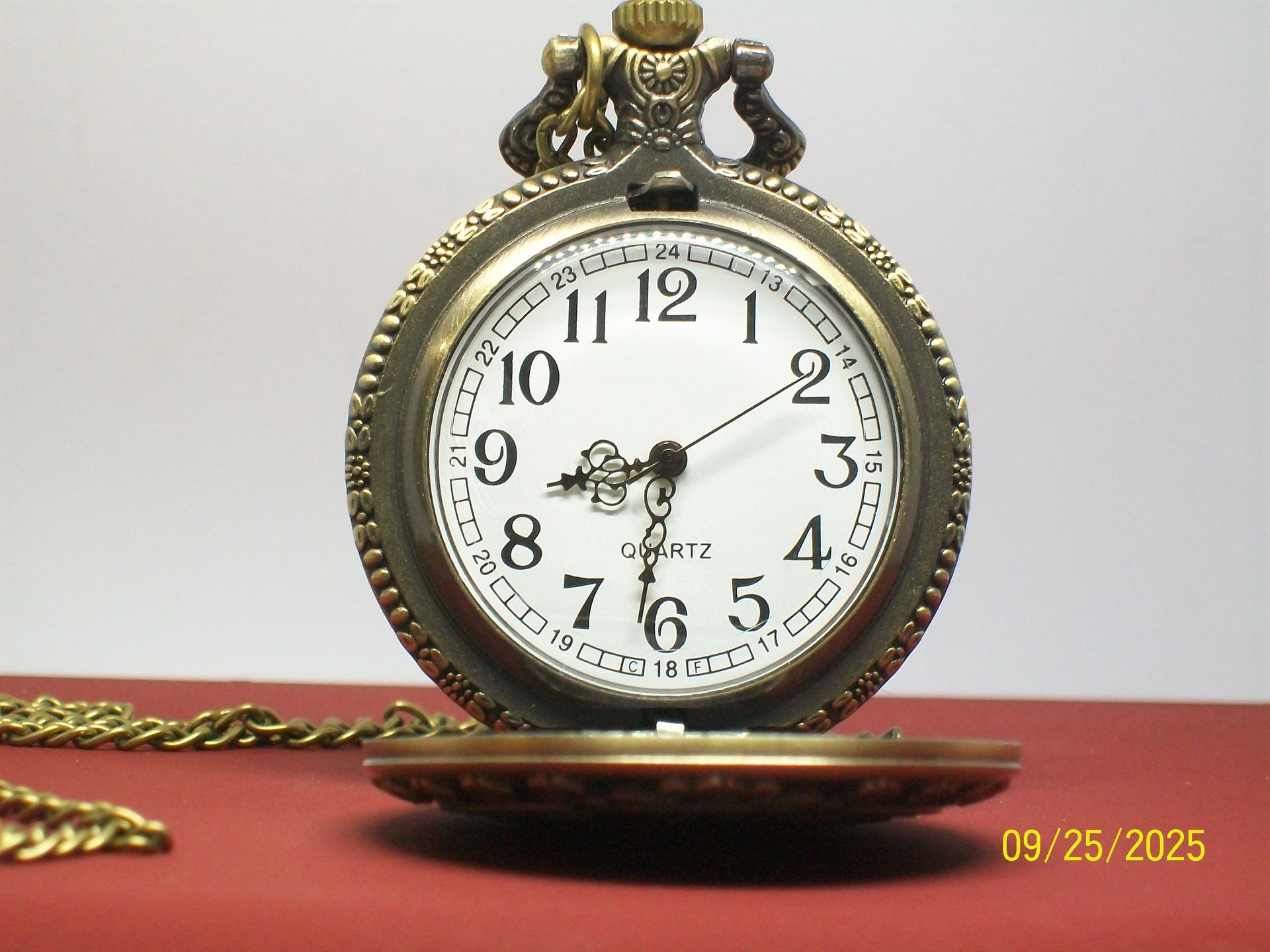 Antiek zakhorloge met open wijzerplaat op een rood oppervlak, met wijzers op 1:14.